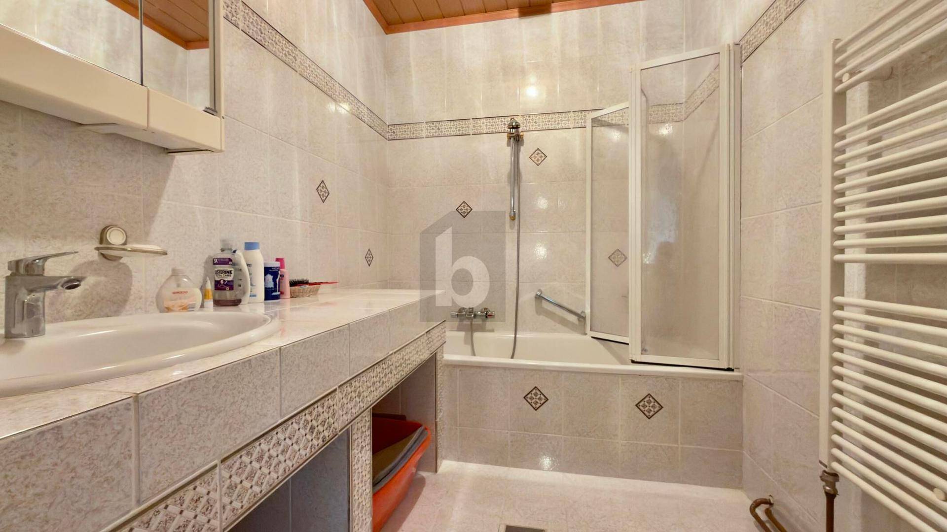 Gefliestes Badezimmer mit Badewanne, Duschabtrennung, Einzelwaschbecken und Handtuchheizkörper.
