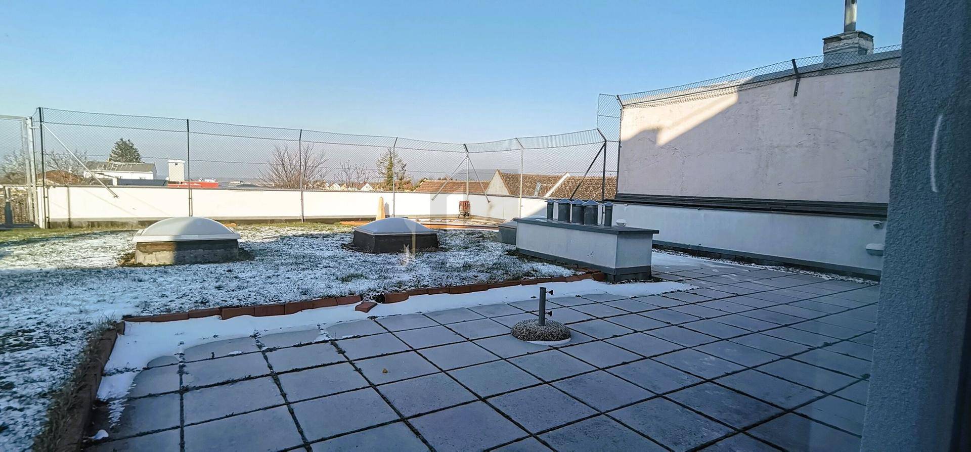Große Dachterrasse mit Fliesenboden und leichter Schneedecke an einem sonnigen Wintertag.