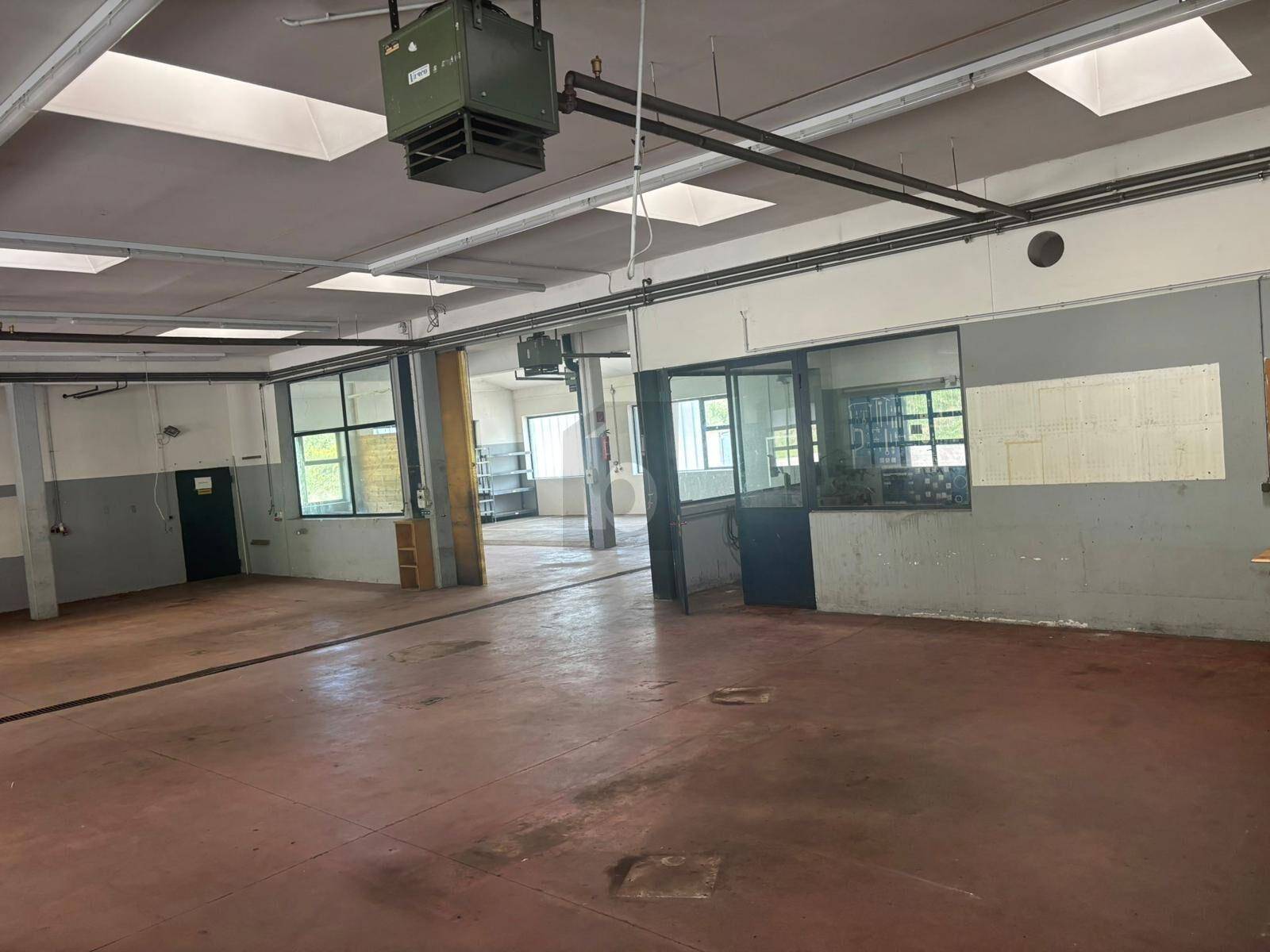 Geräumige Werkstatt oder Lagerhalle mit robustem Boden, Oberlichtern und industrieller Beleuchtung.