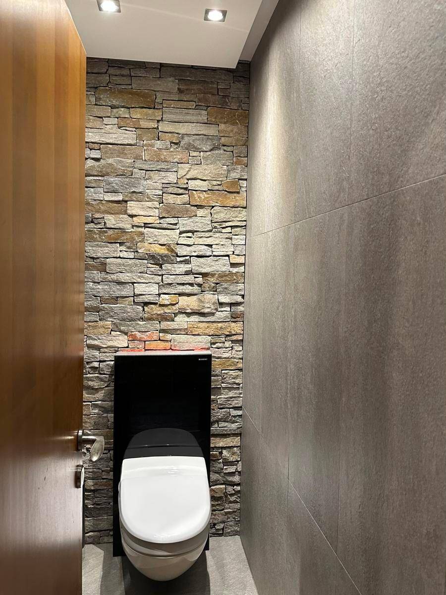 Gäste-WC mit moderner Toilette und dekorativer Steinwand.