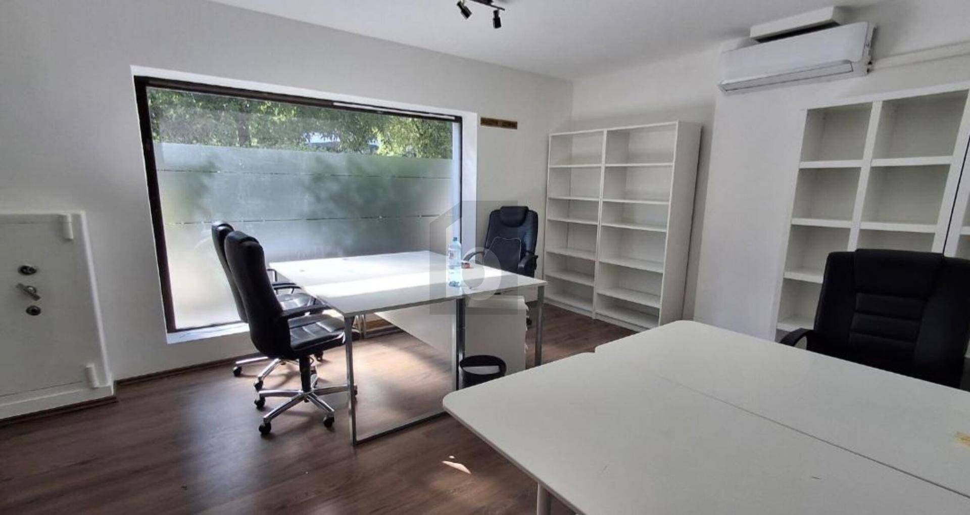 Helles Büro mit großem Fenster, zwei Schreibtischen, Bürostühlen und weißen Regalen, ausgestattet mit Klimaanlage.