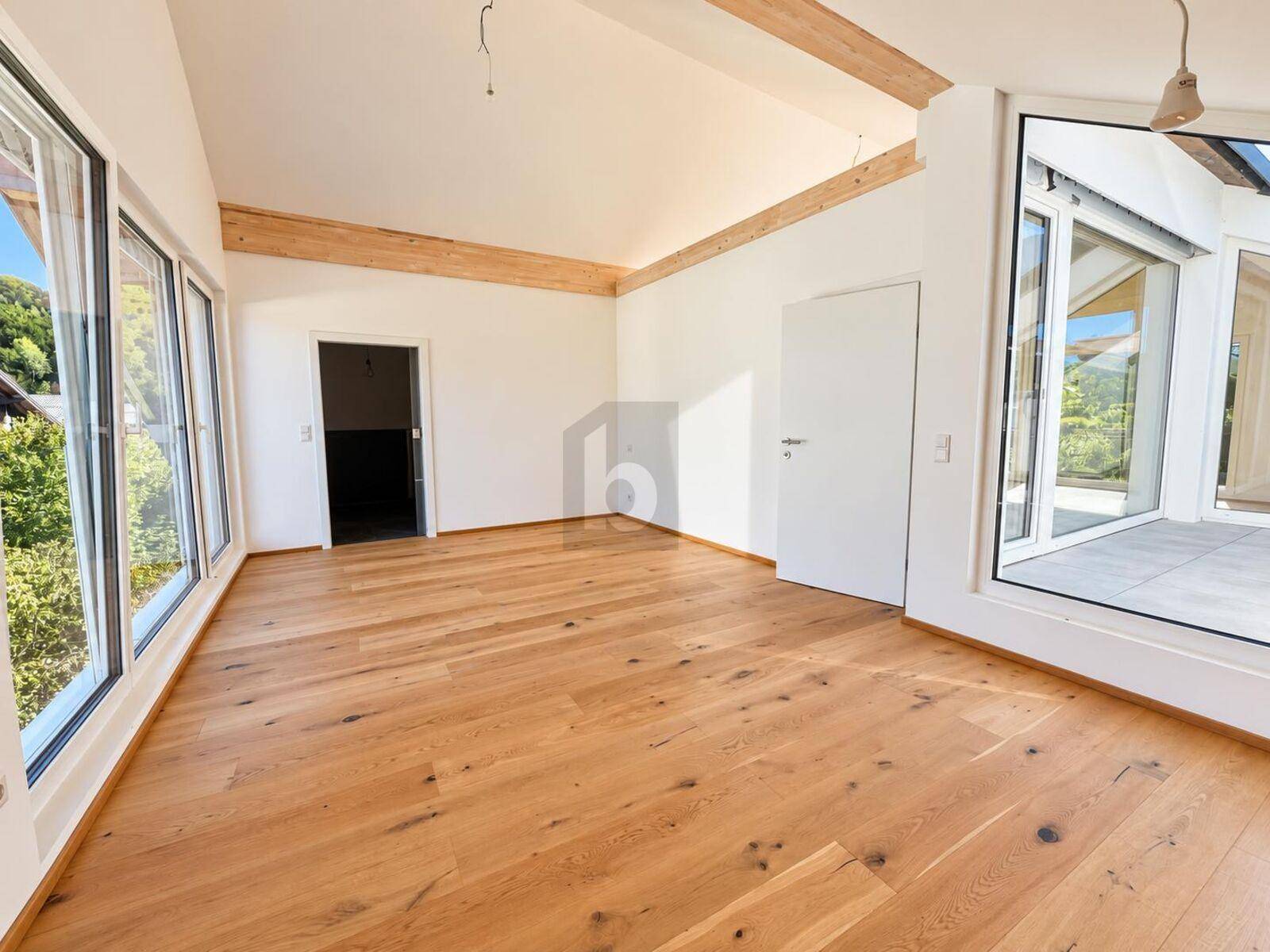 Geräumiger, heller Innenraum mit Holzboden, sichtbaren Deckenbalken und großen Fenstern.
