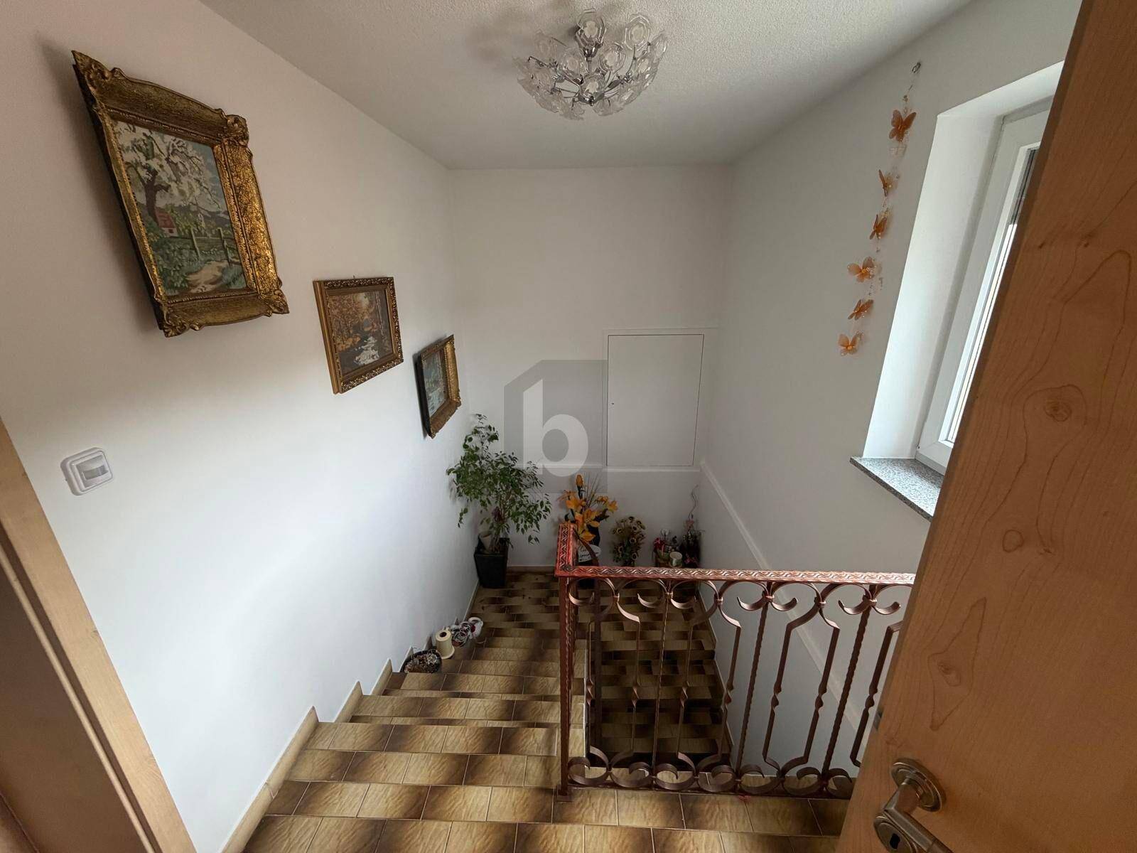 Helles Treppenhaus mit gefliesten Stufen, schmiedeeisernem Geländer und natürlichem Lichteinfall durch ein Fenster.