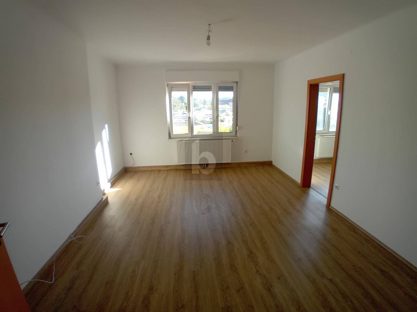 Geräumiges, leeres Zimmer mit Laminatboden und Fenster, das viel Tageslicht hereinlässt.