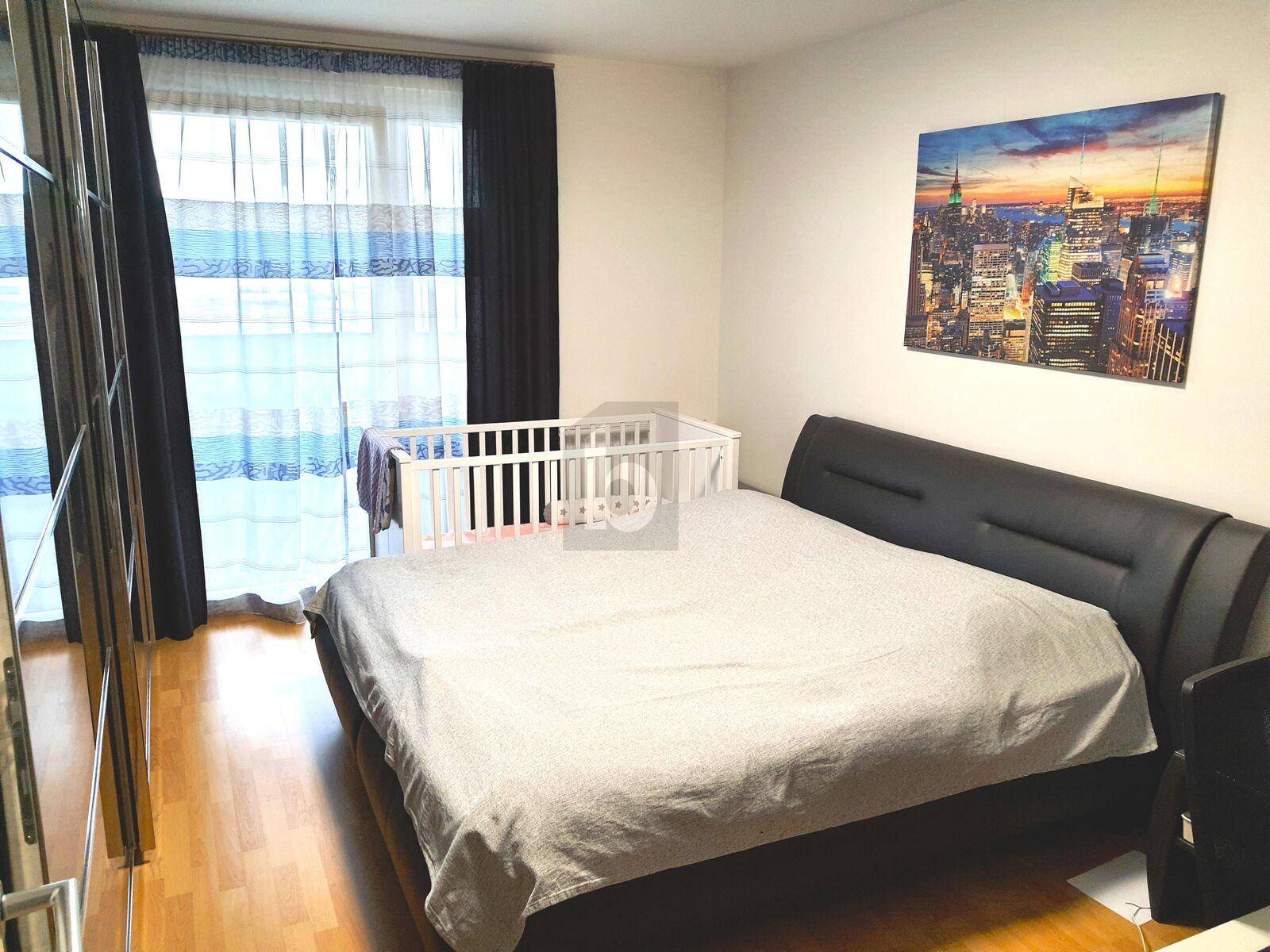 Schlafzimmer mit Doppelbett, Kinderbett und Zugang zu einem Balkon.