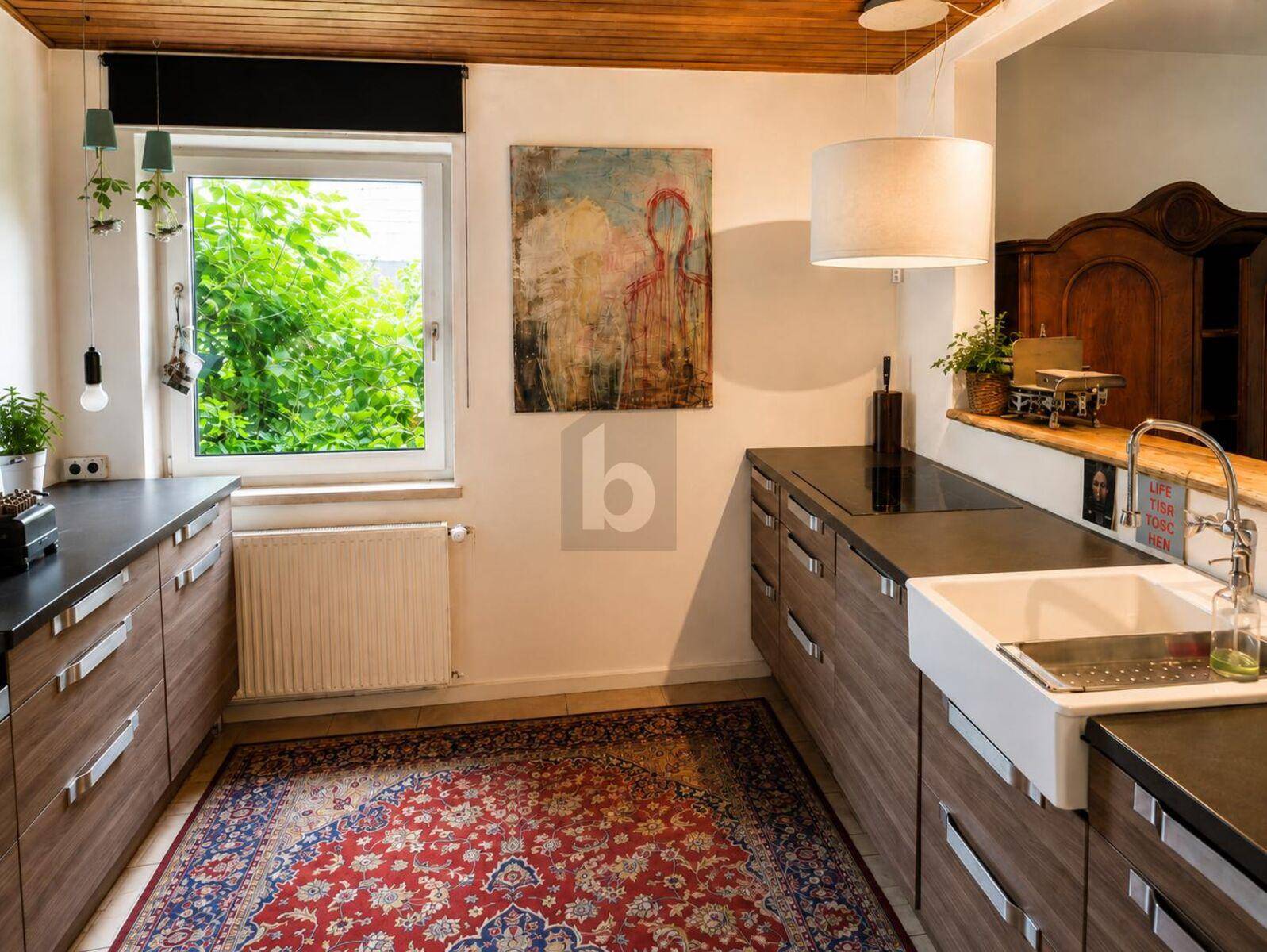 Moderne Küche mit Holzfronten, dunkler Arbeitsplatte, Spülbecken und Fenster mit Grünblick.