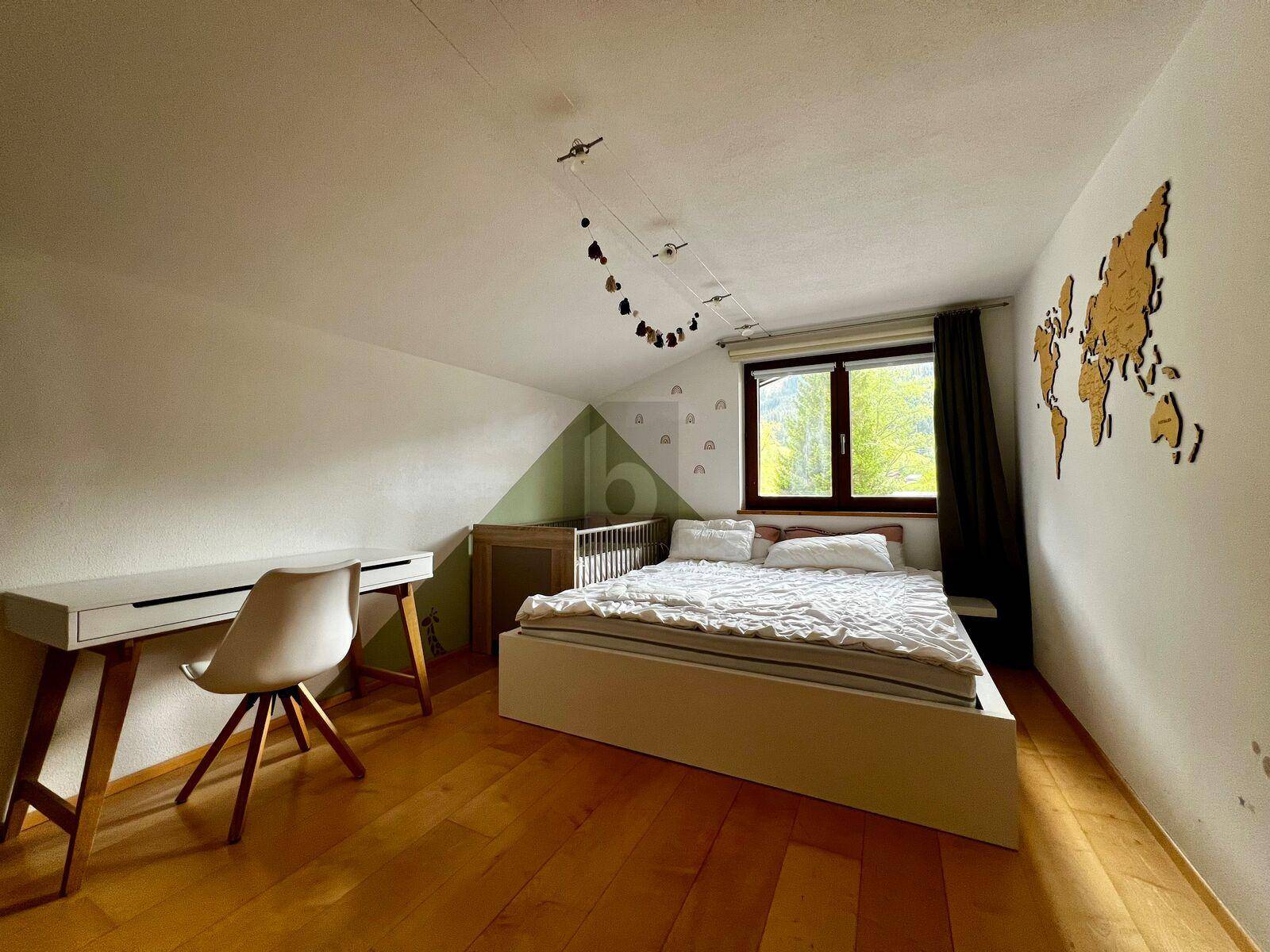 Helles Schlafzimmer im Dachgeschoss mit Holzboden, Schreibtisch und Blick ins Grüne.