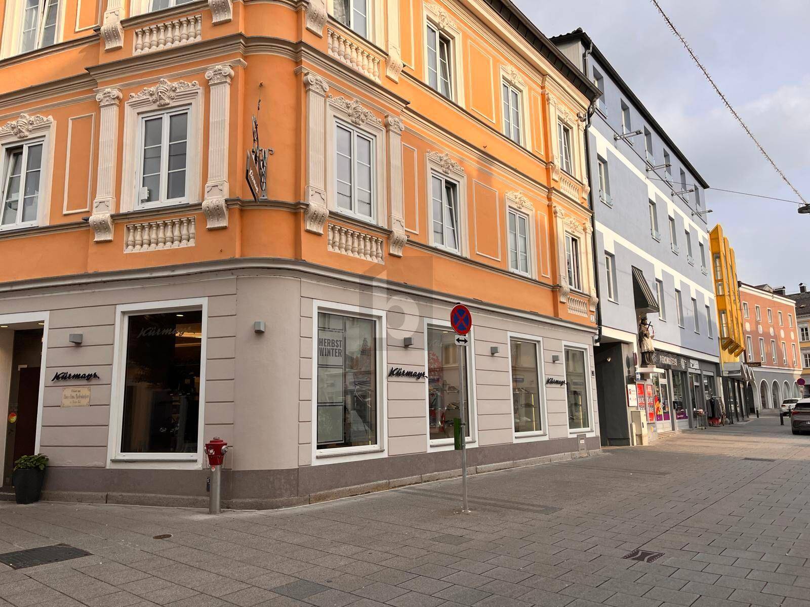 Belebtes Stadtbild mit einem historischen Eckgebäude und angrenzenden Gebäuden an einer Geschäftsstraße.