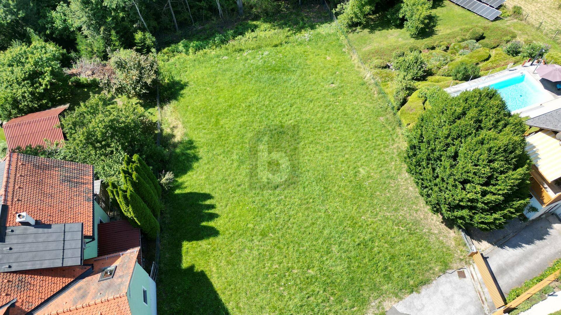 Luftaufnahme eines grünen Grundstücks mit angrenzenden Häusern und einem Pool in der Nachbarschaft.