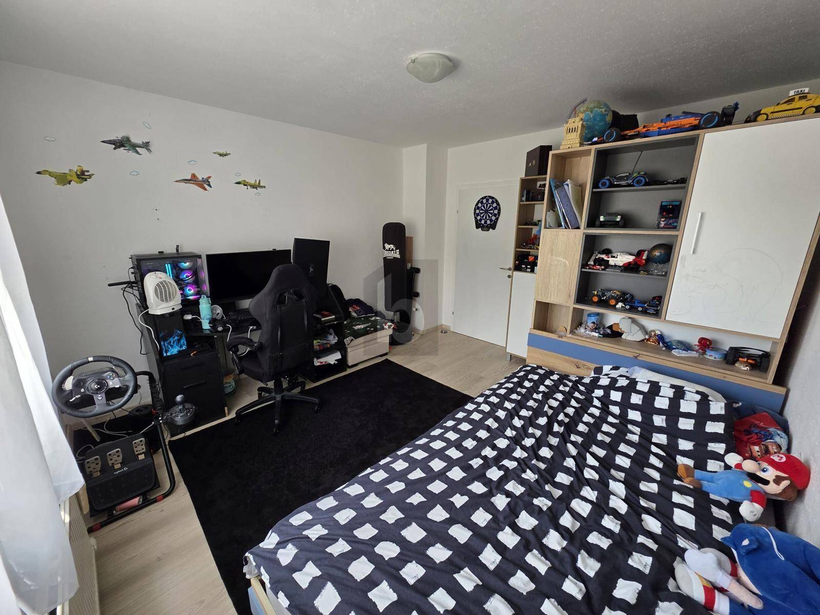 Kinderzimmer mit Gaming-Setup, Schreibtisch und Stauraum für Spielzeug und Bücher.
