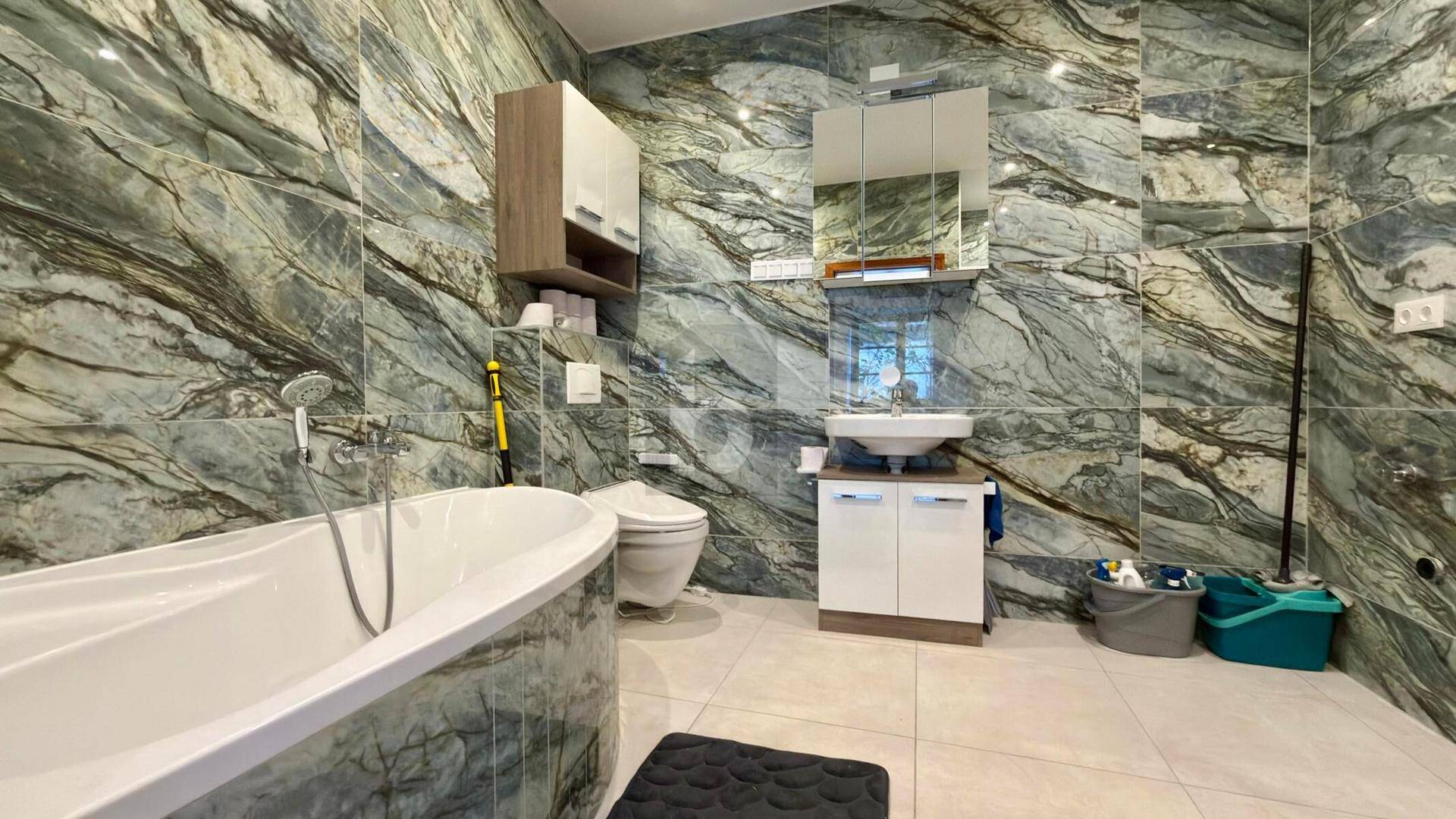 Geräumiges Badezimmer mit auffälligen grünen Marmorfliesen, freistehender Badewanne und Einzelwaschbecken.