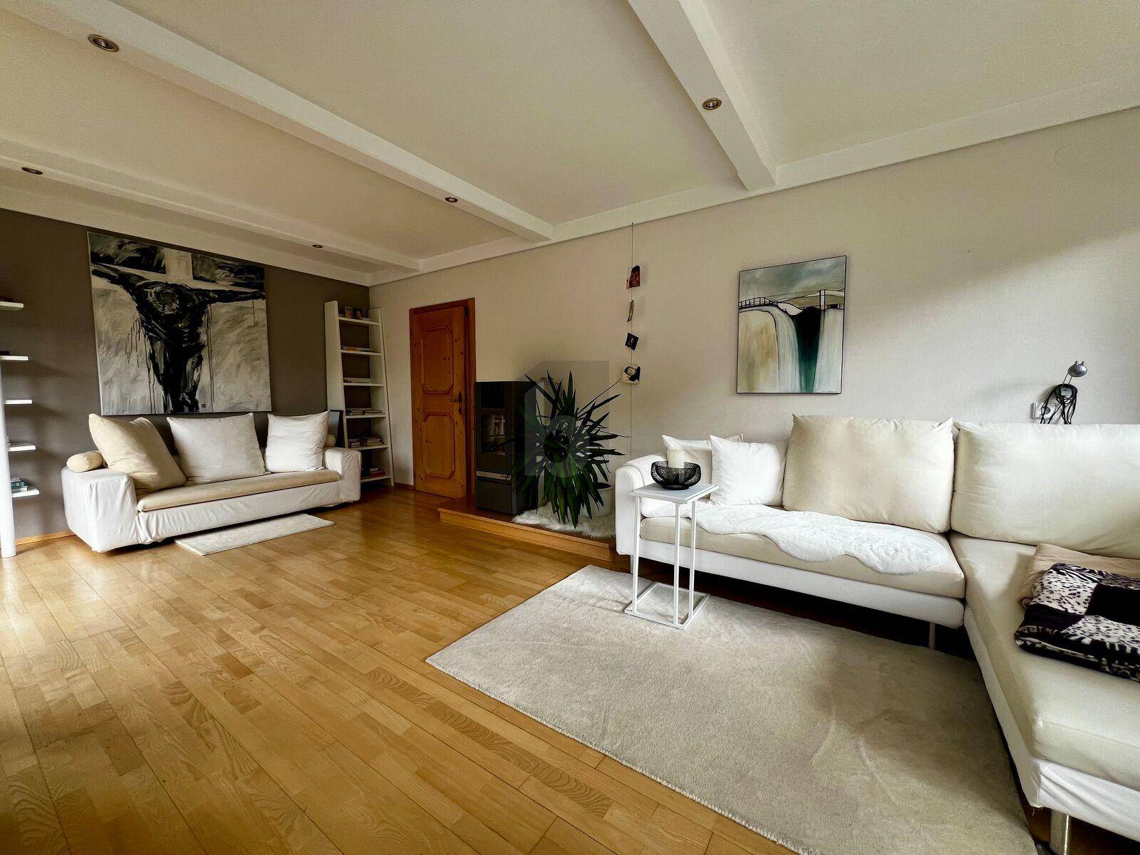 Gemütliches Wohnzimmer mit hellem Holzboden, bequemen Sofas und einem modernen Kaminofen.
