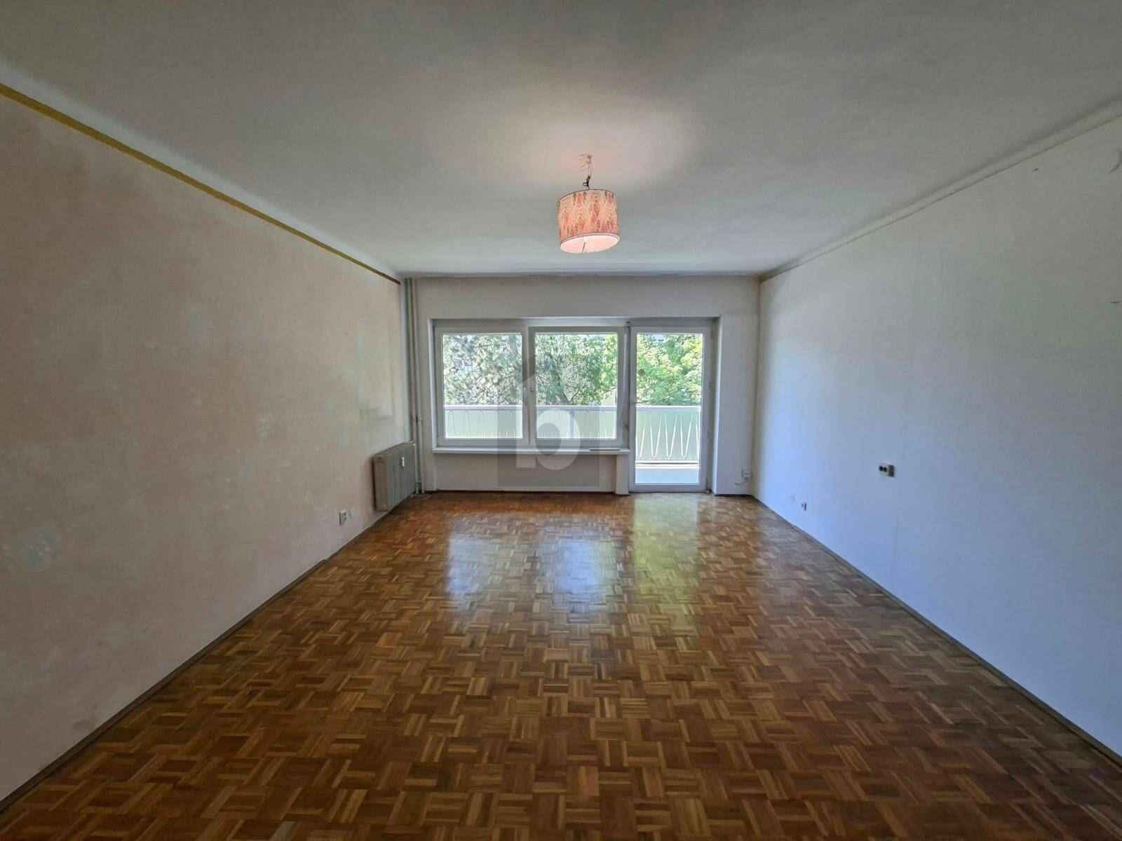 Geräumiges Wohnzimmer mit klassischem Parkettboden und Zugang zu einem Balkon.