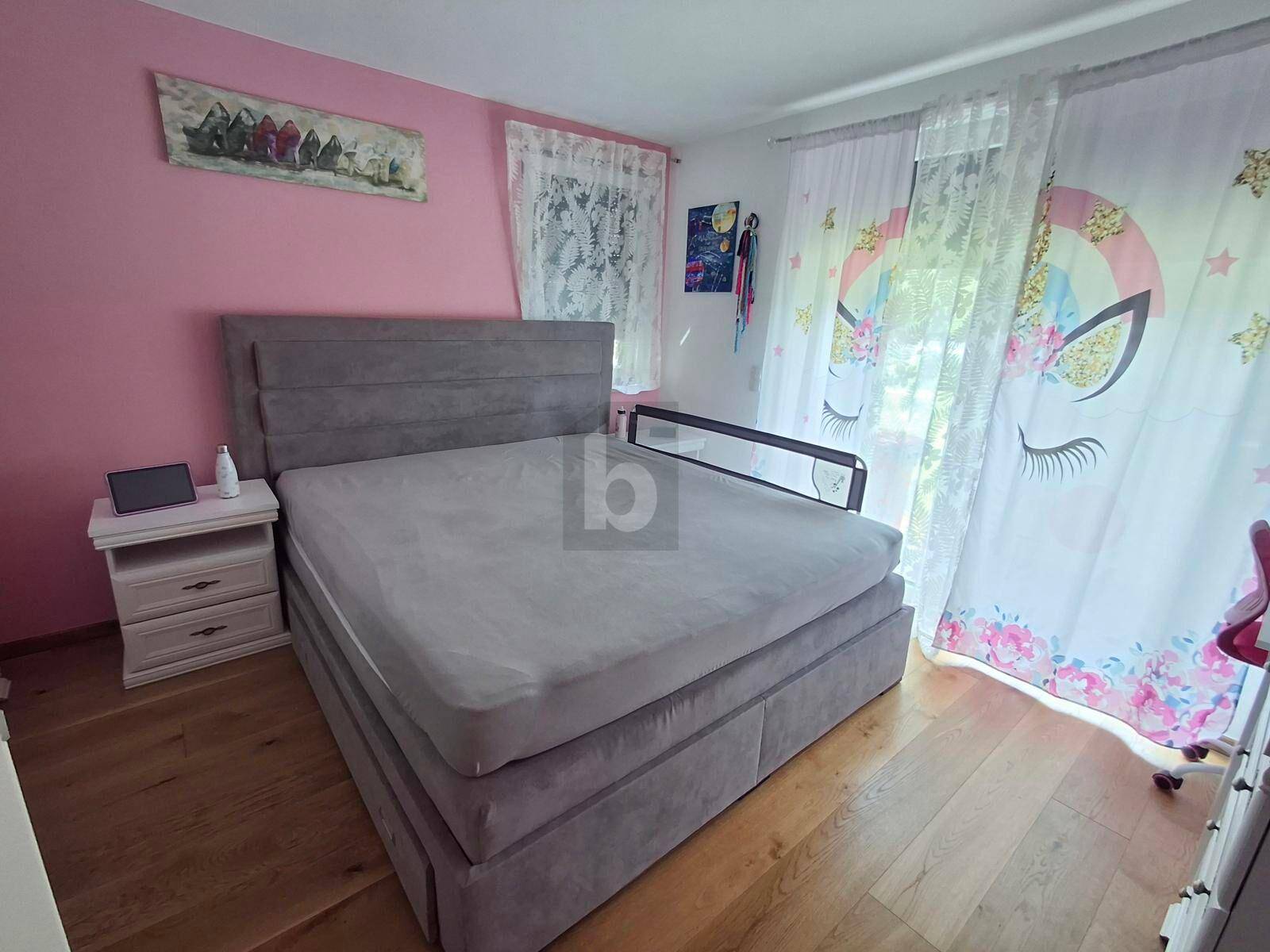 Gemütliches Schlafzimmer mit großem Bett, rosa Wand und farbenfrohen Vorhängen.