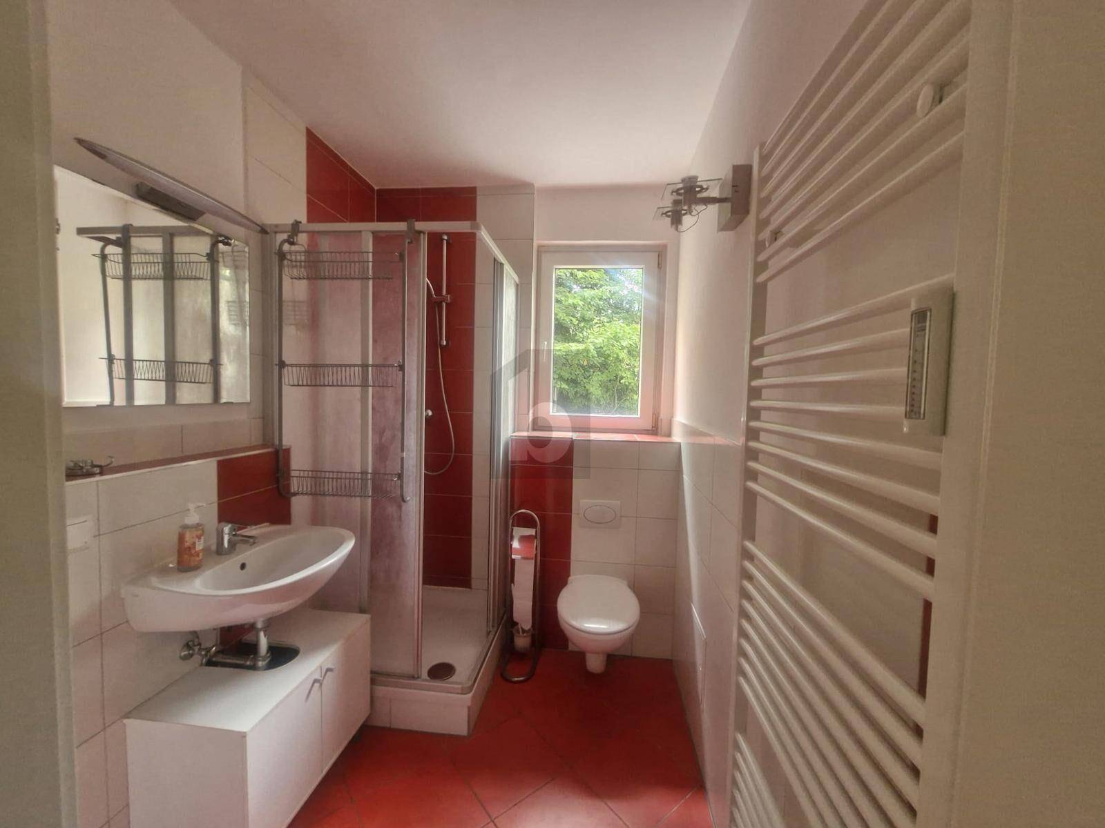 Badezimmer mit Dusche, Waschbecken, WC und roten Fliesen.