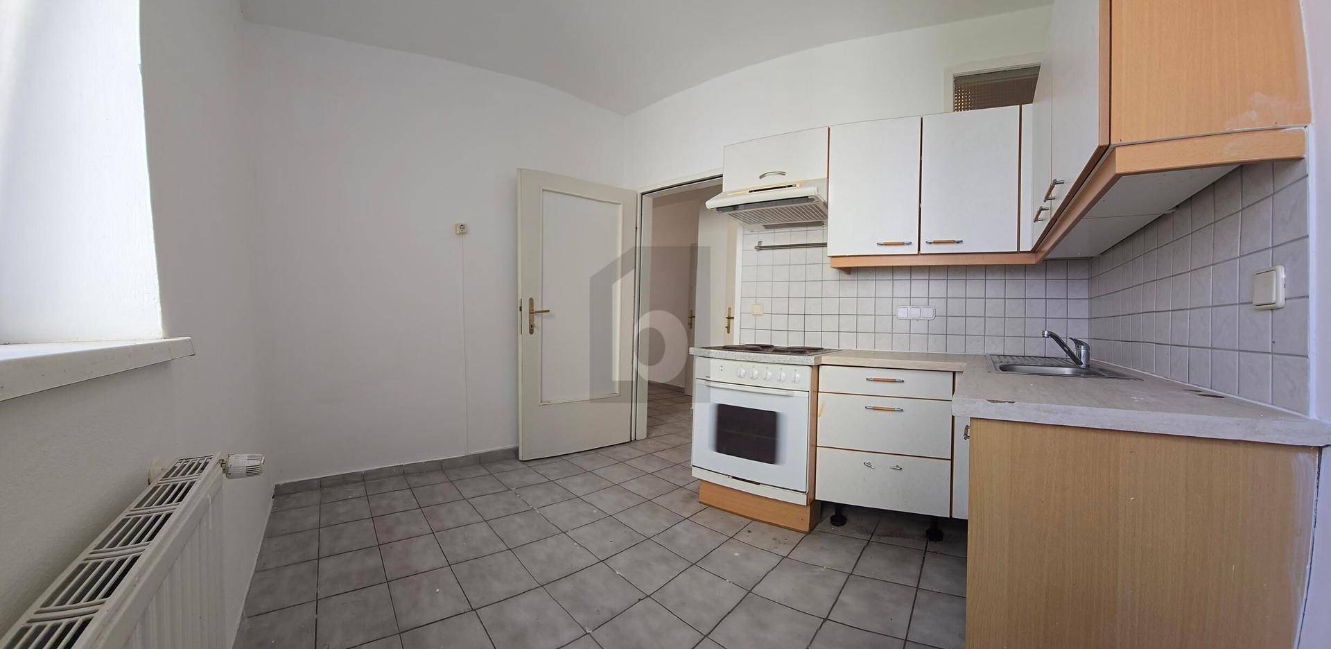 Küche mit Einbauschränken, Herd und Spüle, sowie einem gefliesten Boden und Fenster.