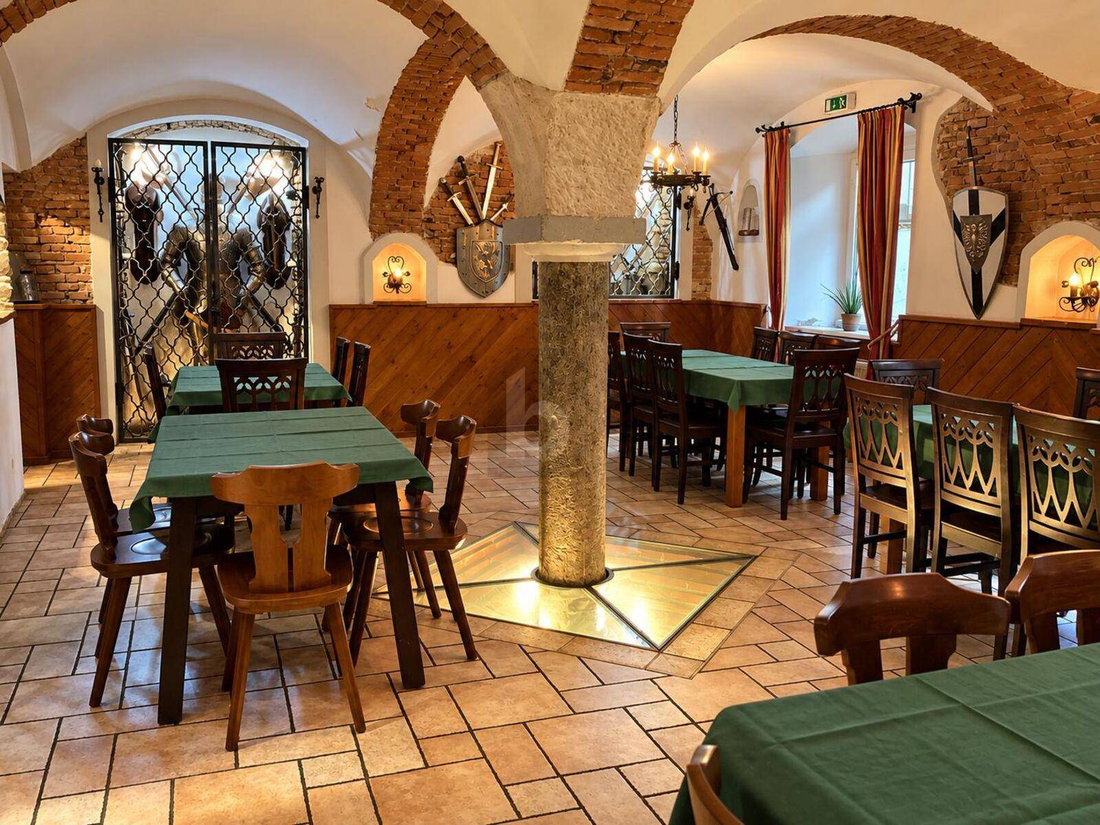 Rustikaler Speisesaal im Keller mit freiliegenden Ziegelgewölben, Steinsäulen und mittelalterlicher Dekoration.