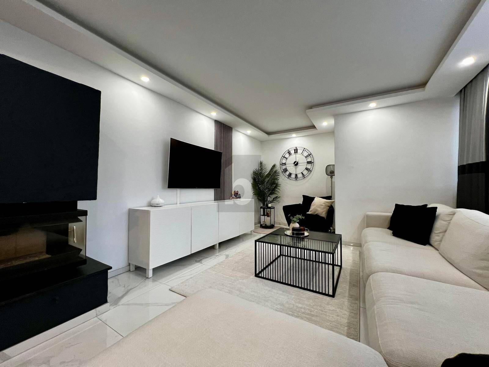 Helles Wohnzimmer mit modernem Sofa, Couchtisch, großem Wandfernseher und stilvoller Dekoration.