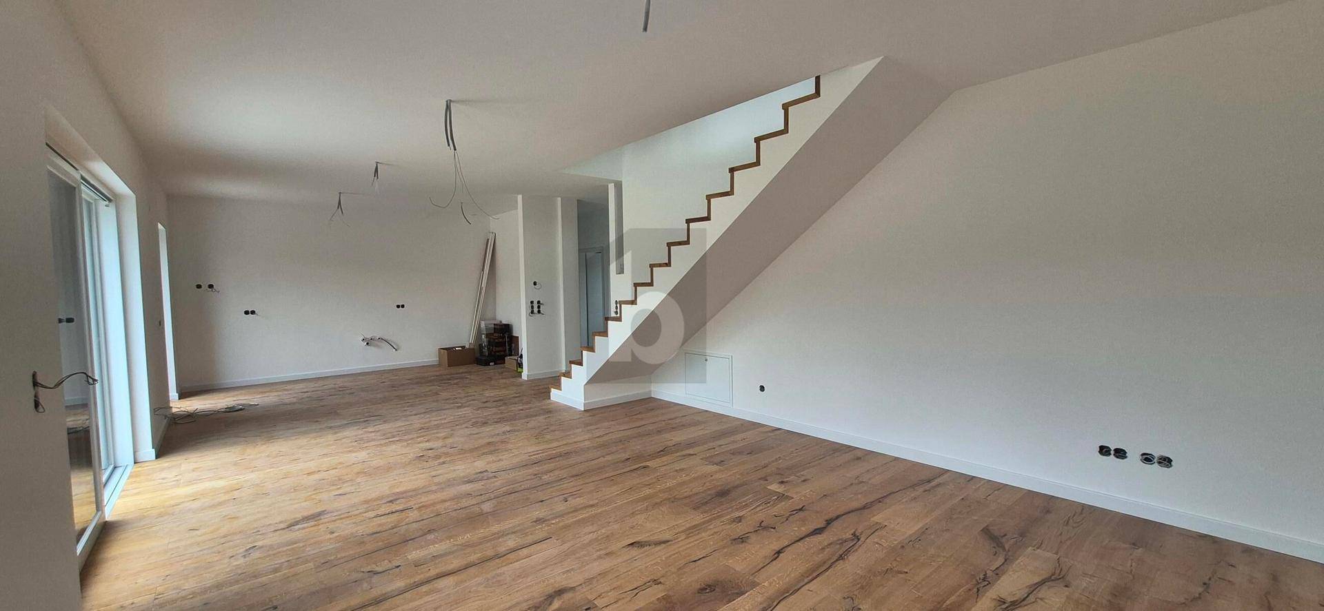 Geräumiger Wohnbereich mit Holzboden und moderner Treppe im Neubau.