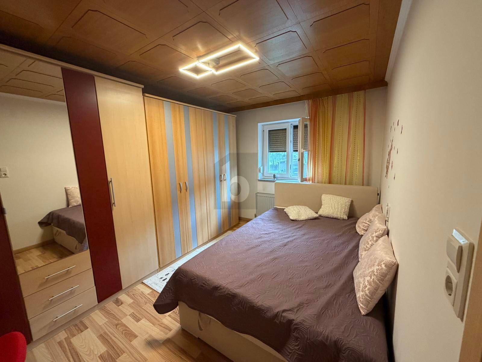 Gemütliches Schlafzimmer mit Doppelbett, Holzdecke und Einbauschränken, hell durch das Fenster.