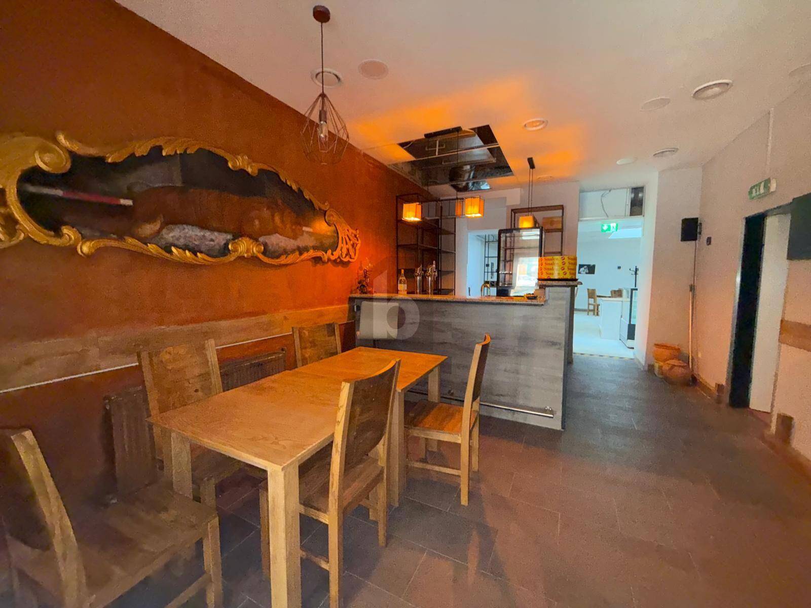 Gemütlicher Barbereich mit orangefarbener Wand, Holztischen und einer Theke, ideal für gesellige Runden.