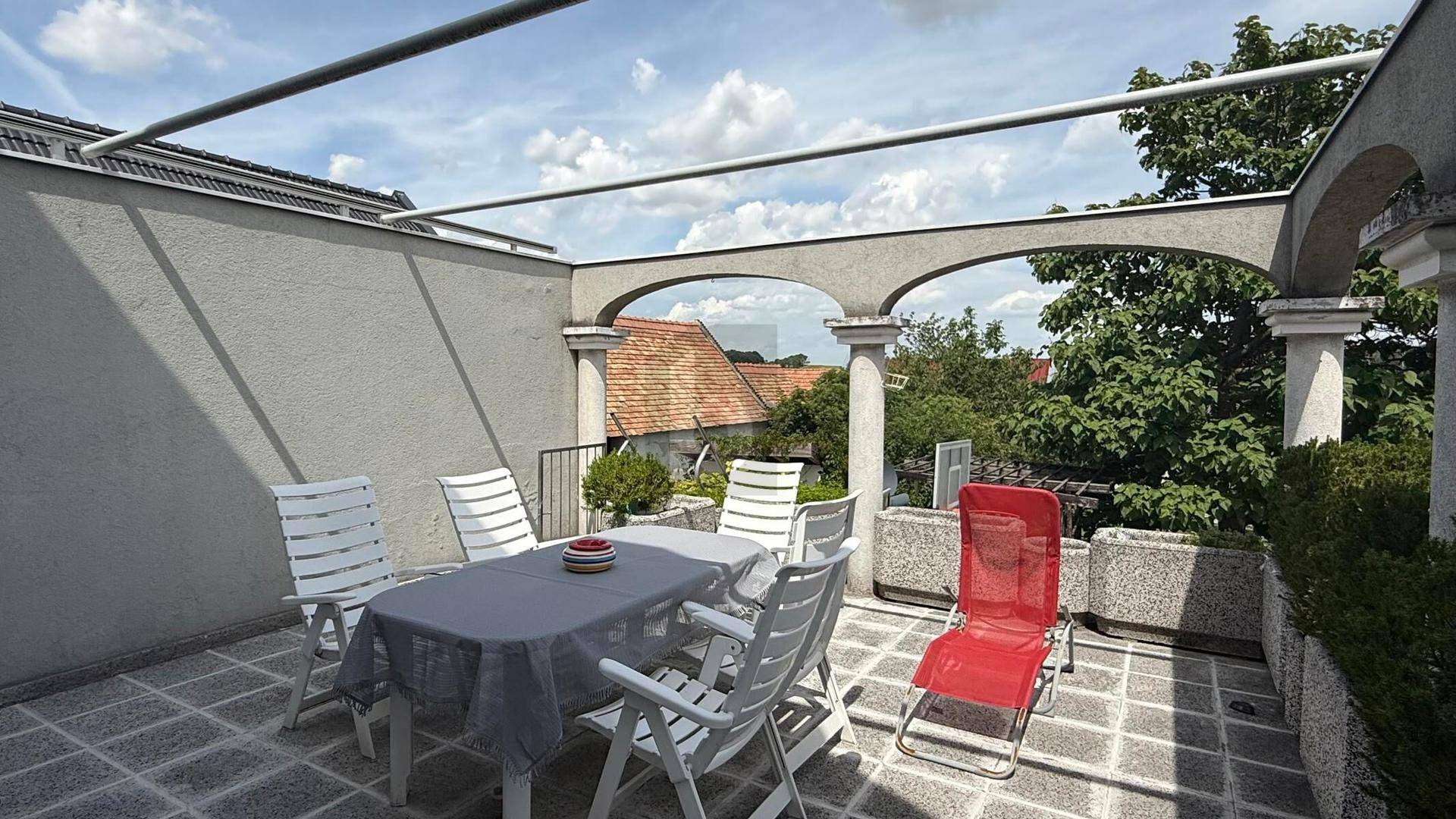 Geflieste Dachterrasse mit Esstisch, Gartenmöbeln und dekorativen Bögen.