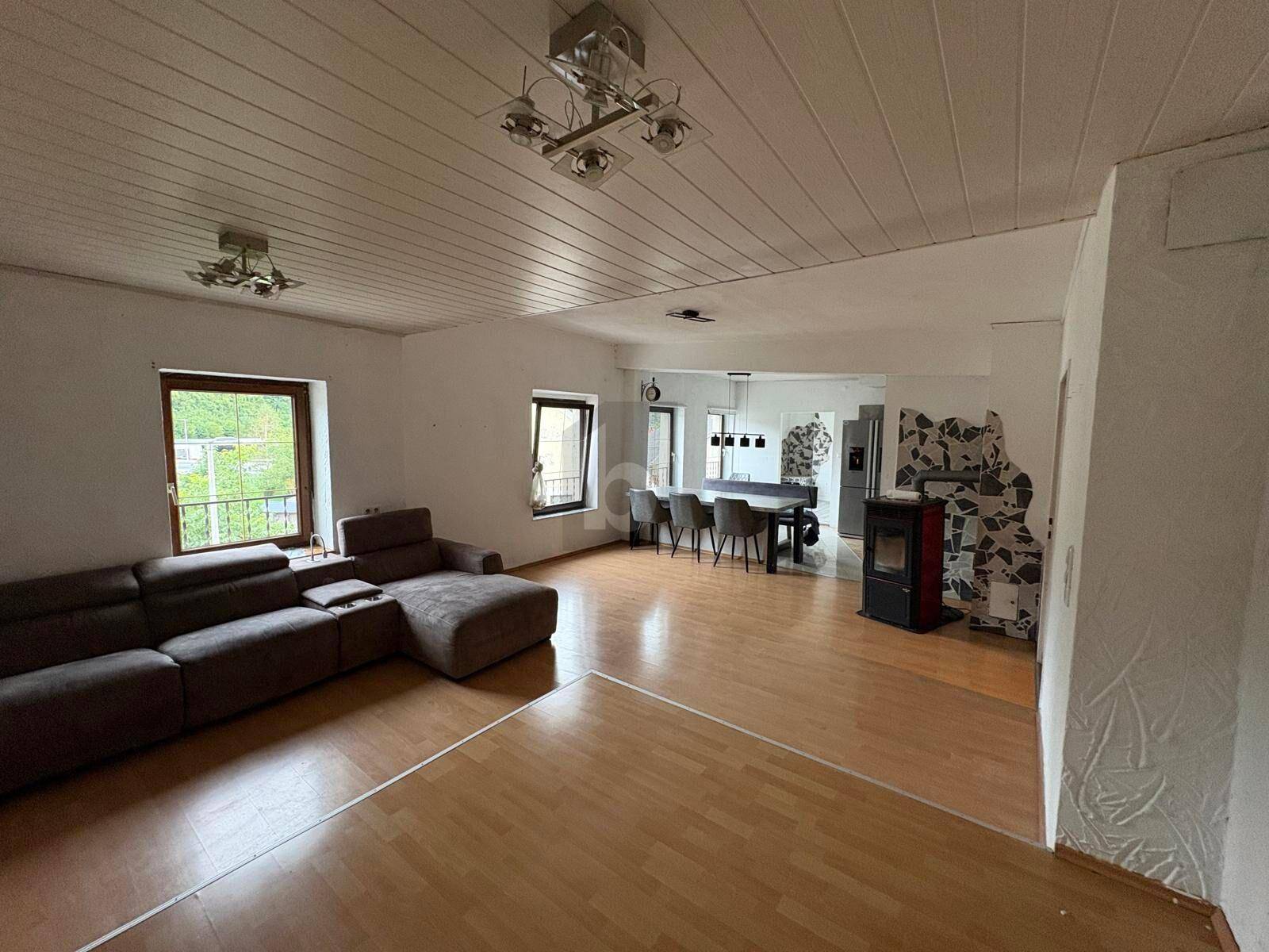 Großer offener Wohn- und Essbereich mit Holzboden, gemütlichem Sofa und Kaminofen.