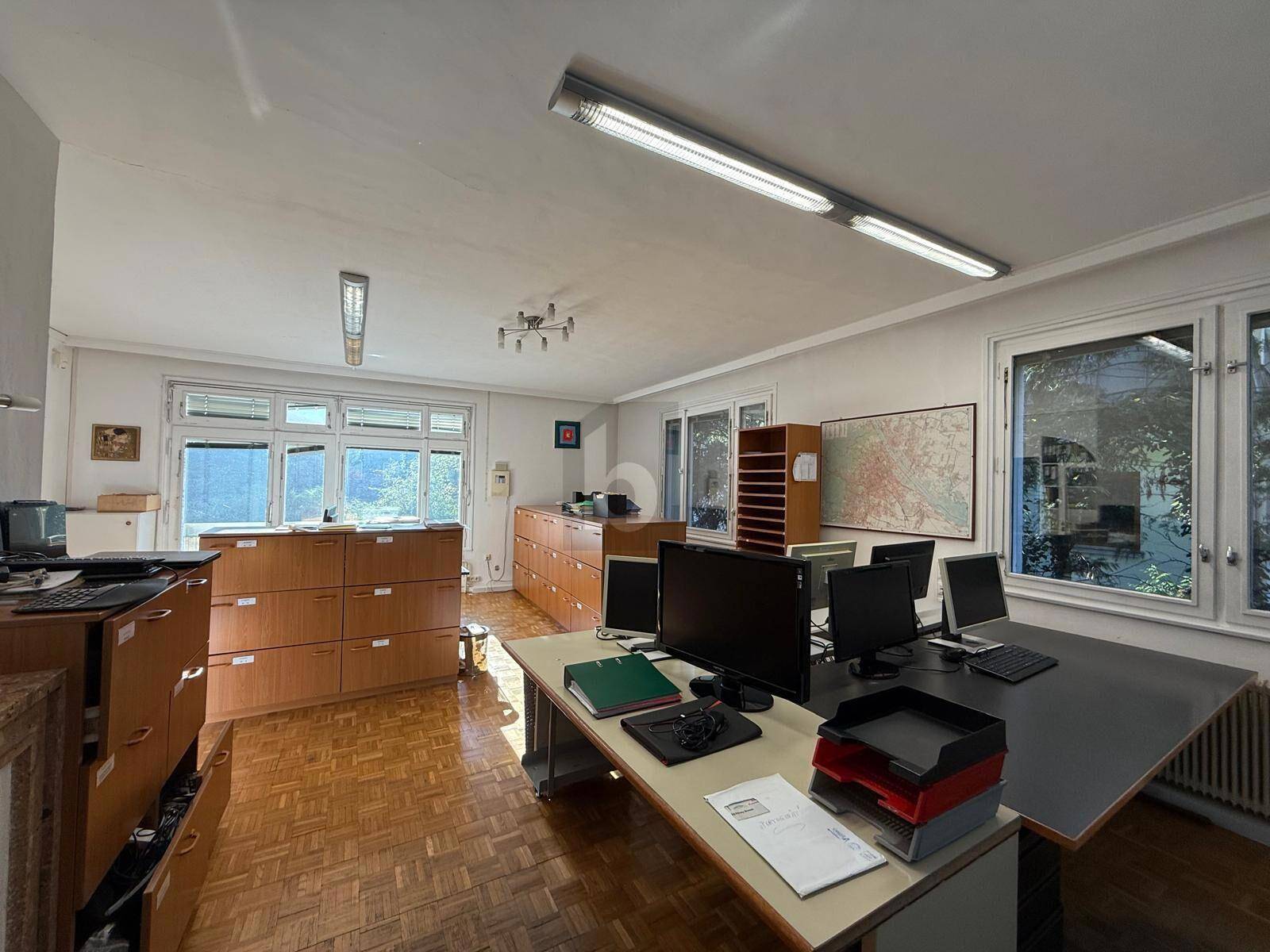 Helles und funktionales Büro mit mehreren Arbeitsplätzen, Holzmöbeln und großen Fenstern mit Blick ins Grüne.