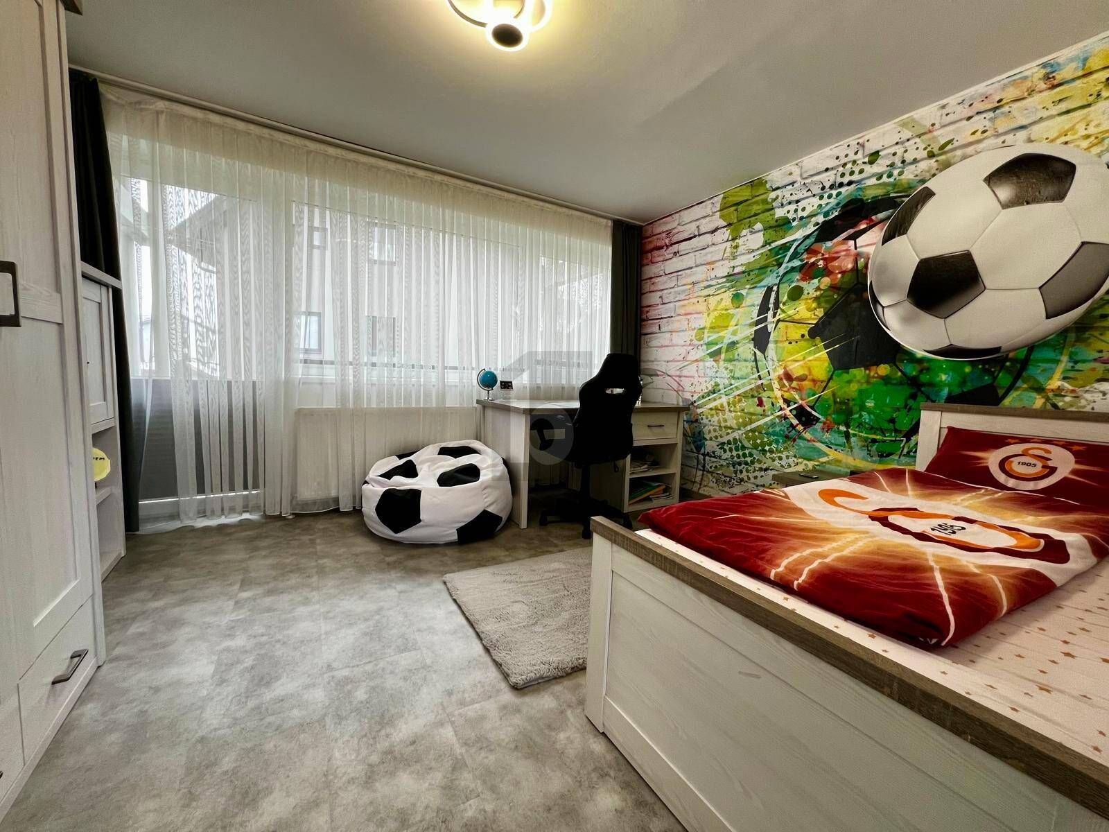 Kinderzimmer mit kreativer Fußball-Wanddekoration, Bett und Schreibtisch am großen Fenster.
