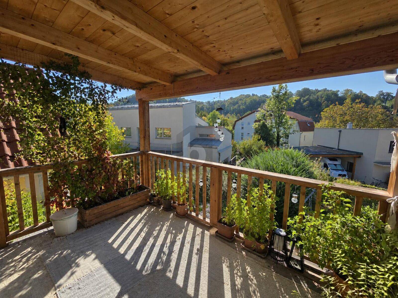 Überdachter Holzbalkon mit Pflanzen und Blick ins Grüne, ideal für entspannte Stunden im Freien.