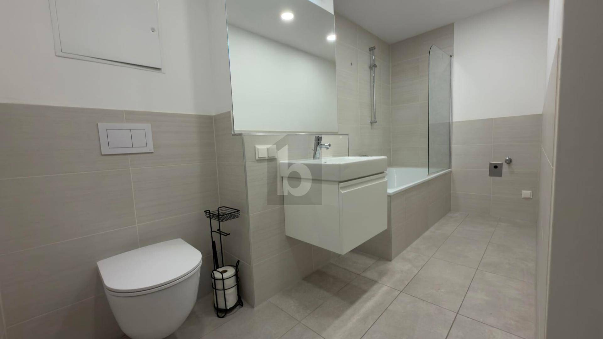 Modernes Badezimmer mit hellgrauen Fliesen, Badewanne mit Duschwand und wandhängendem WC.