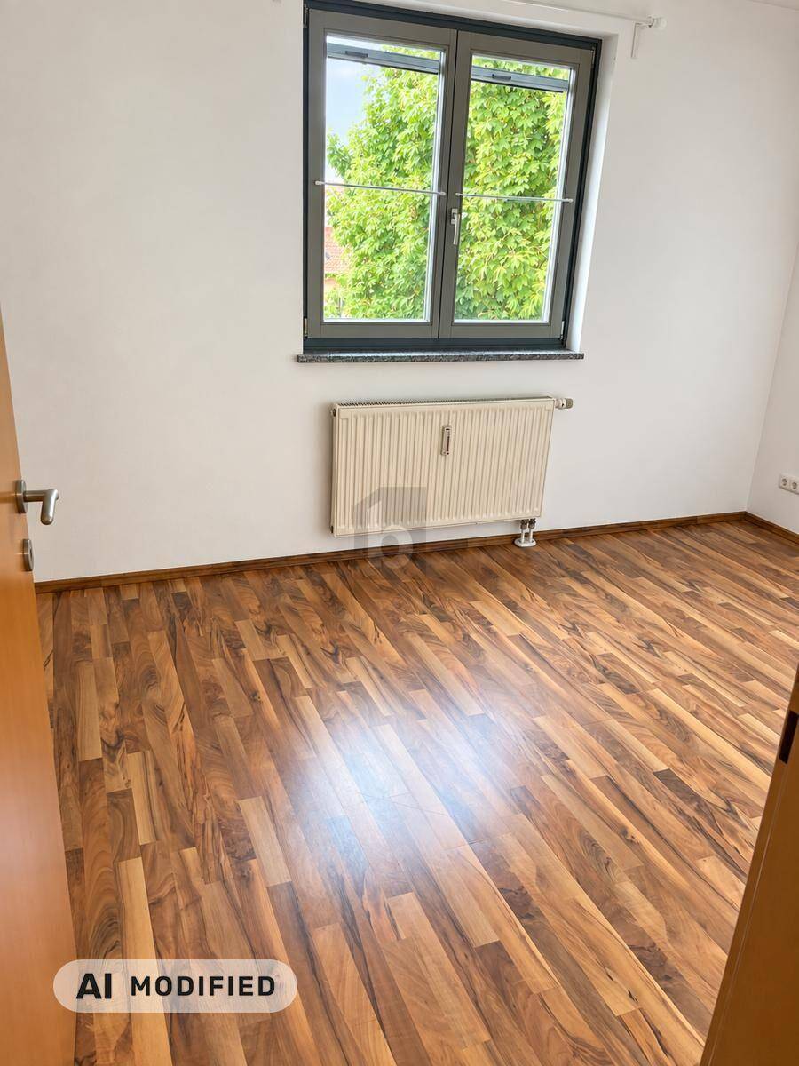 Leeres Zimmer mit Laminatboden, weißen Wänden und Fenster mit Blick ins Grüne.