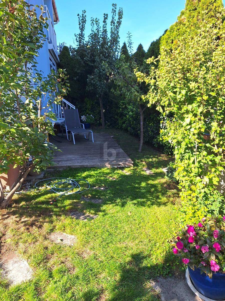 Grüner Gartenbereich mit Rasenfläche, Holzterrasse und üppiger Bepflanzung.