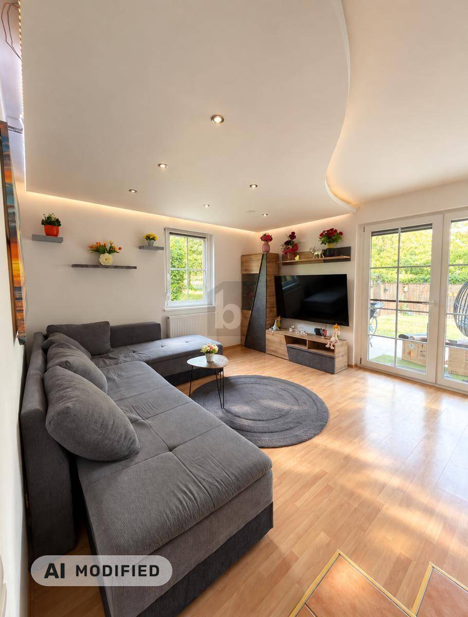 Helles Wohnzimmer mit großem Ecksofa, Fernseher und Zugang zur Terrasse.