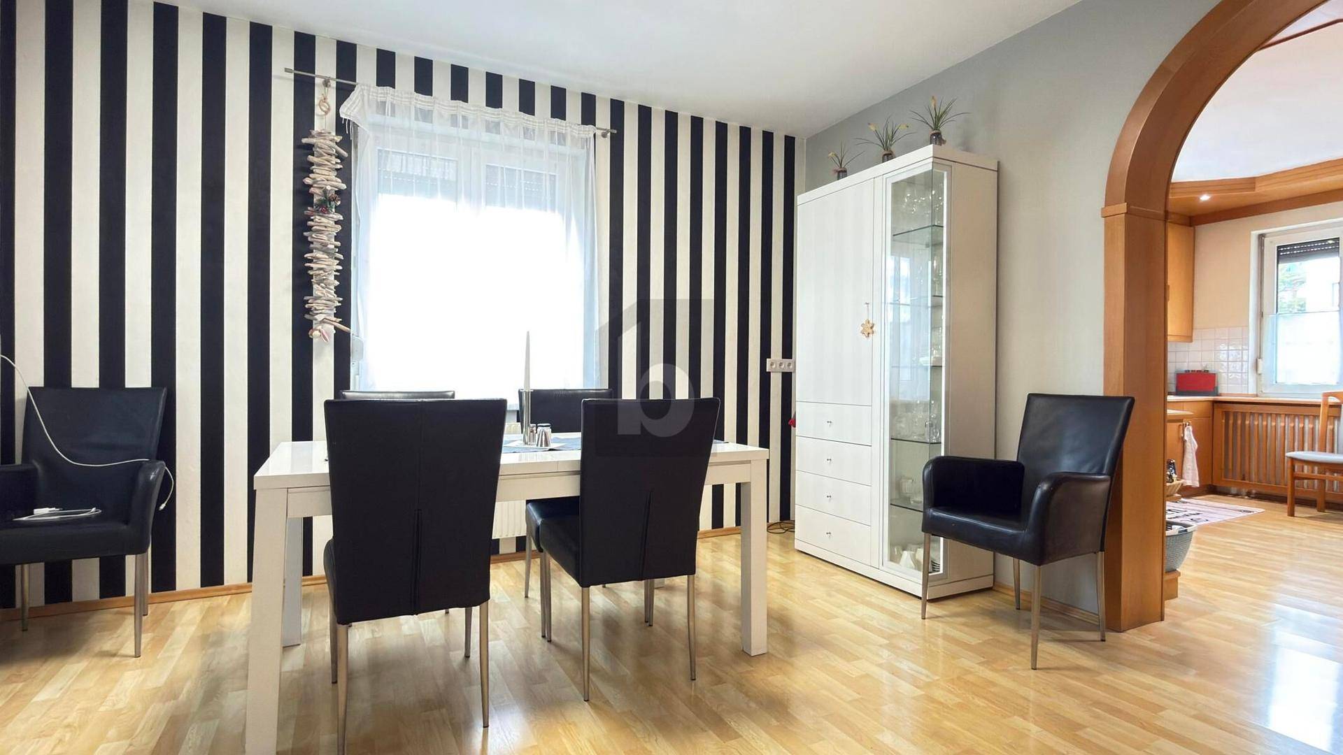 Esszimmer mit markanter schwarz-weiß gestreifter Tapete, Holztisch und Zugang zur Küche.