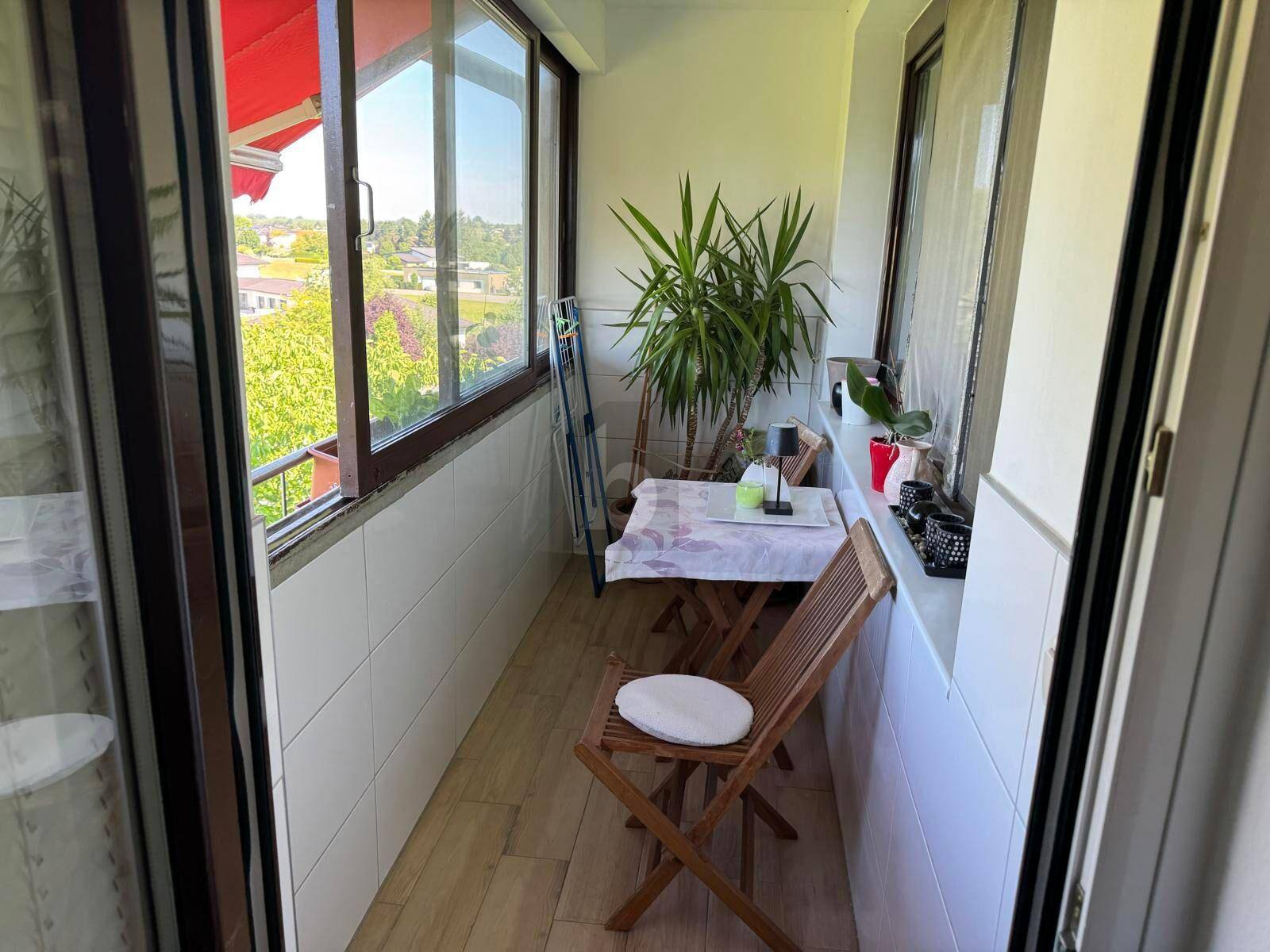 Verglaste Loggia mit Holztisch, Stühlen und Pflanzen, bietet einen schönen Ausblick.