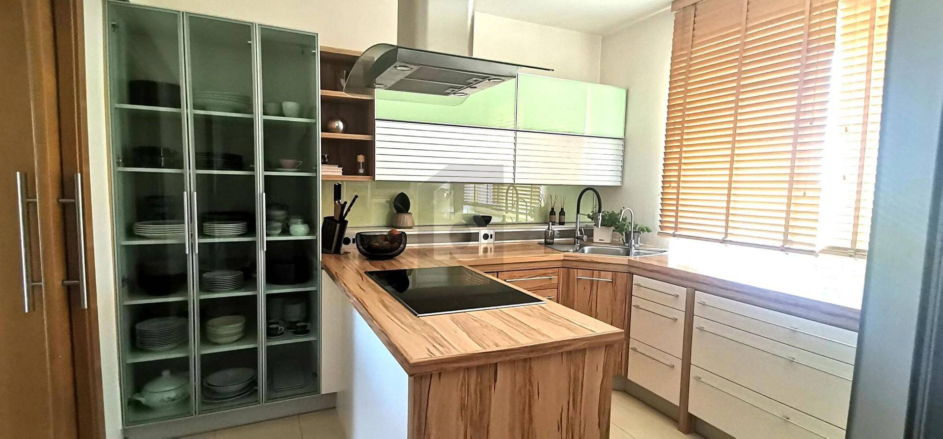 Moderne Küche mit Holz-Arbeitsplatten, grünen Oberschränken und integriertem Kochfeld.