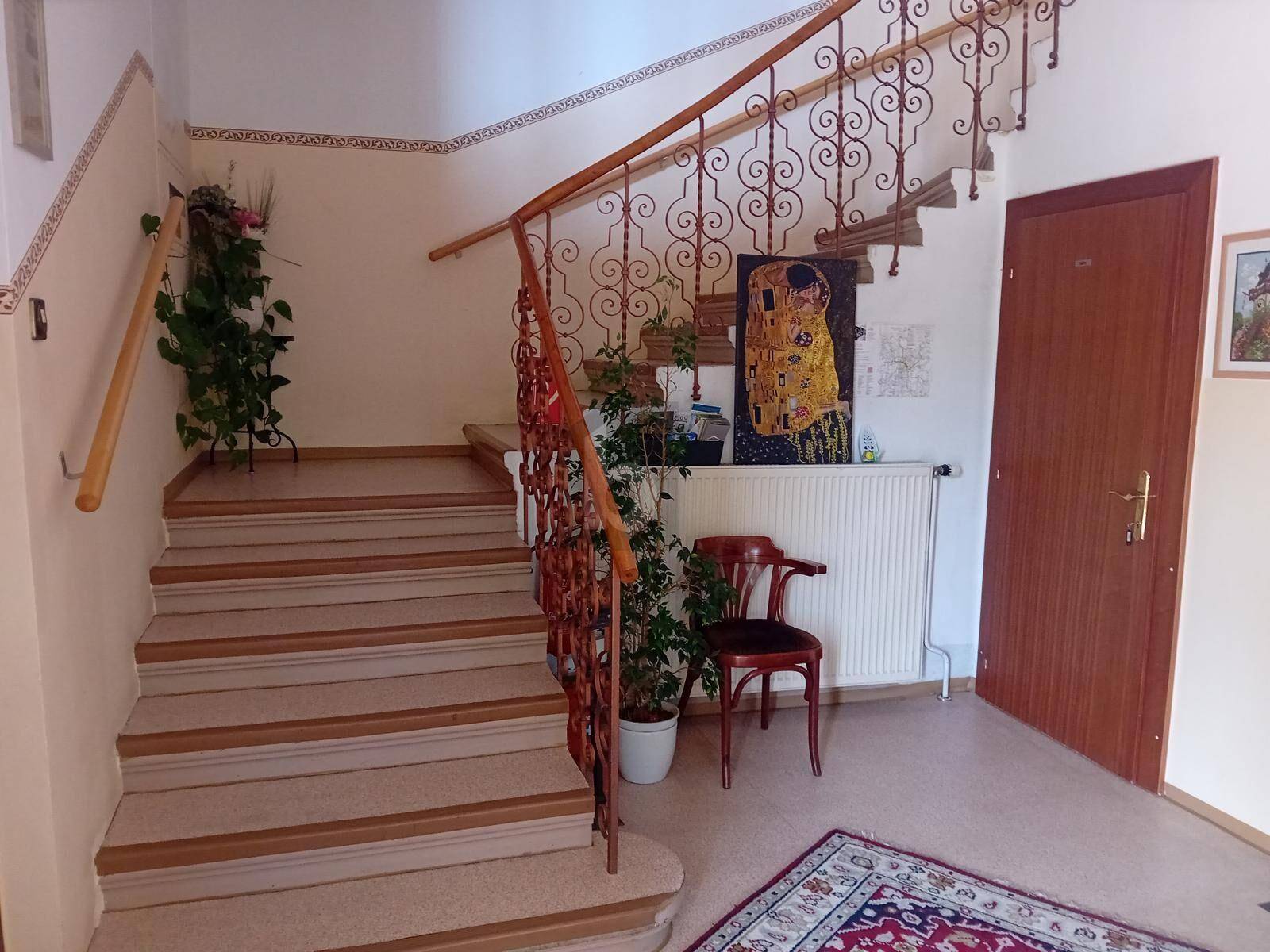 Elegantes Treppenhaus mit schmiedeeisernem Geländer, Holzstufen und dekorativem Kunstwerk im Eingangsbereich.