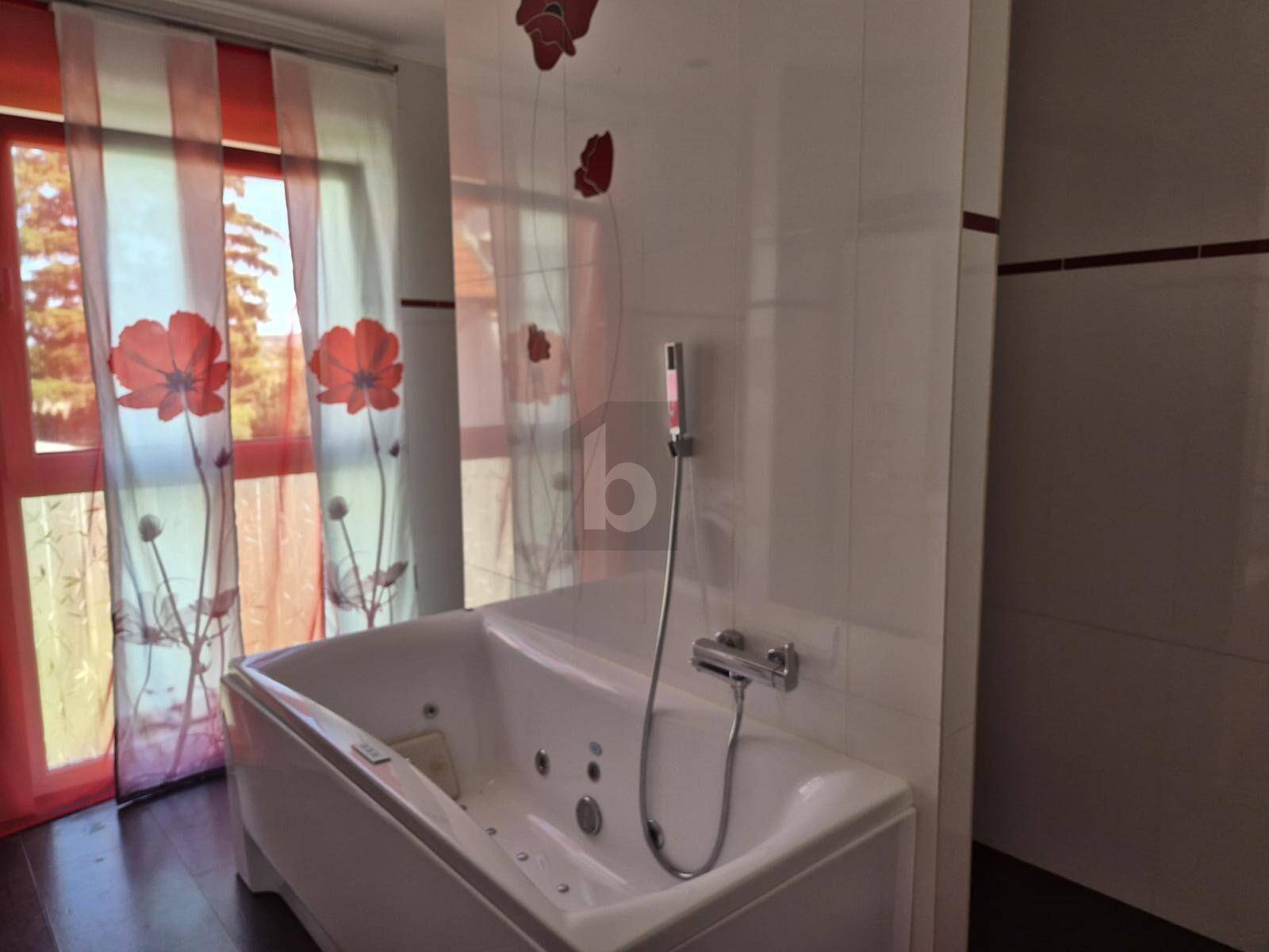 Badezimmer mit moderner Badewanne und Fenster, dekoriert mit roten floralen Vorhängen.