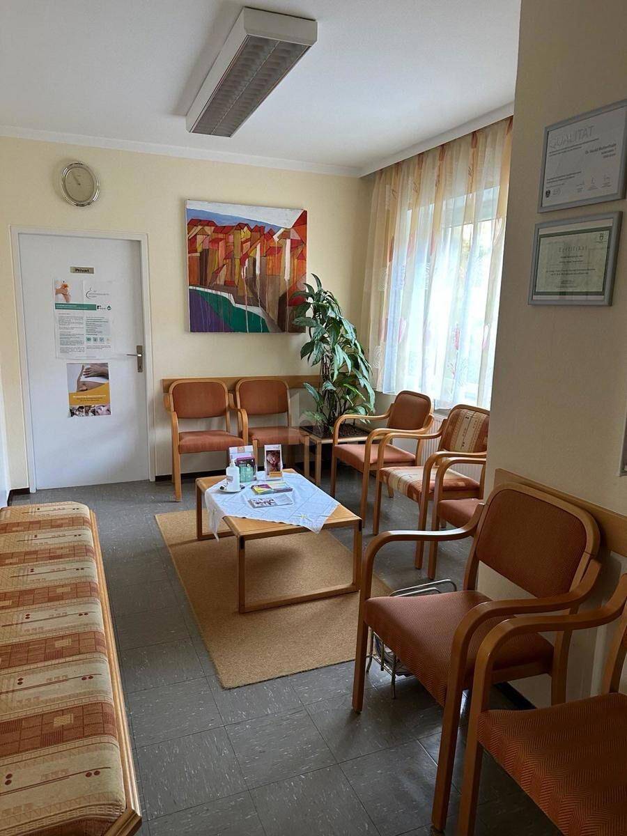 Gemütlicher Wartebereich mit mehreren Holzstühlen, einem Couchtisch und einem dekorativen Gemälde.