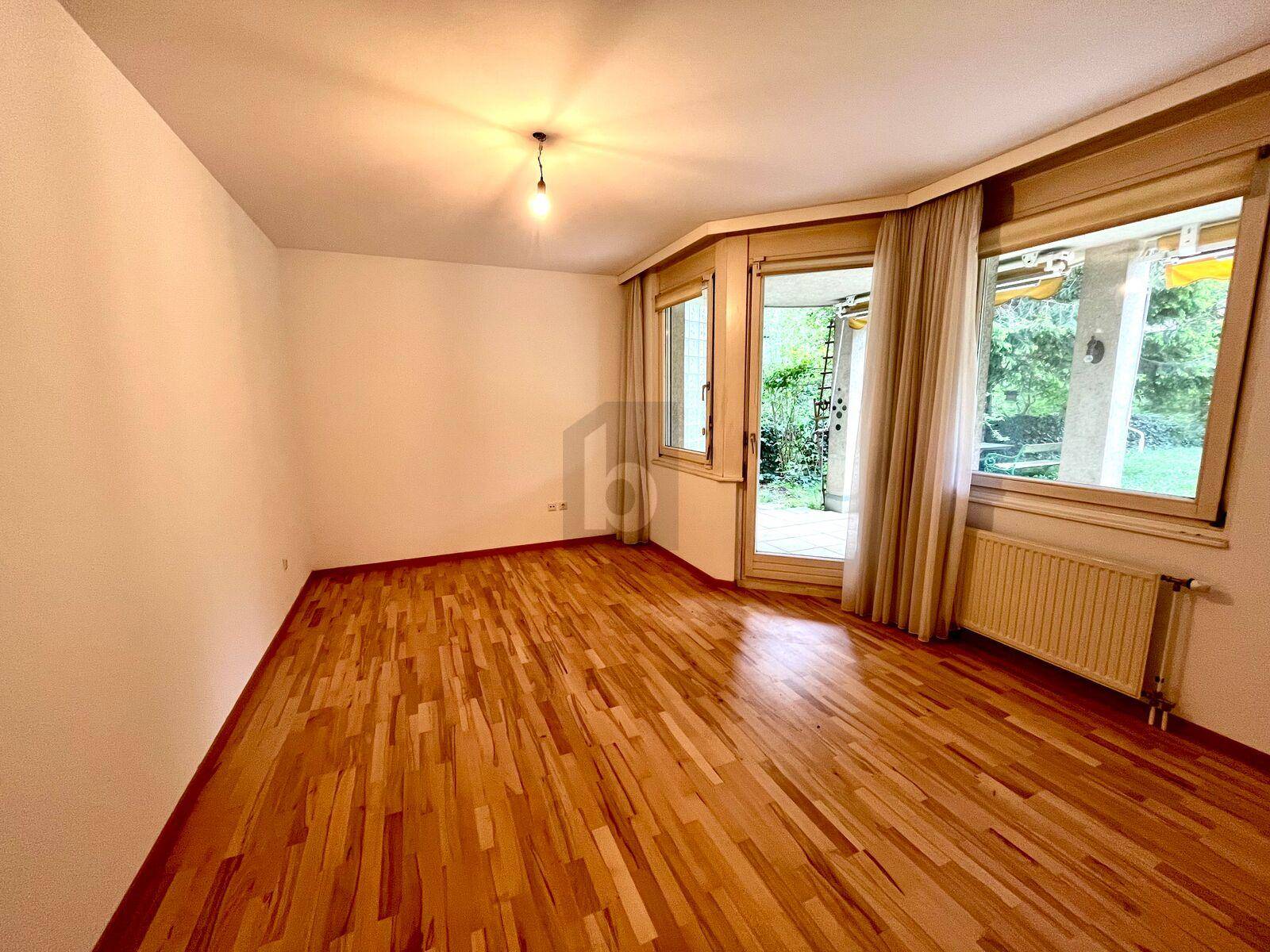Geräumiges Zimmer mit hellem Parkettboden und einer Glastür, die den Zugang zu einem Außenbereich ermöglicht.