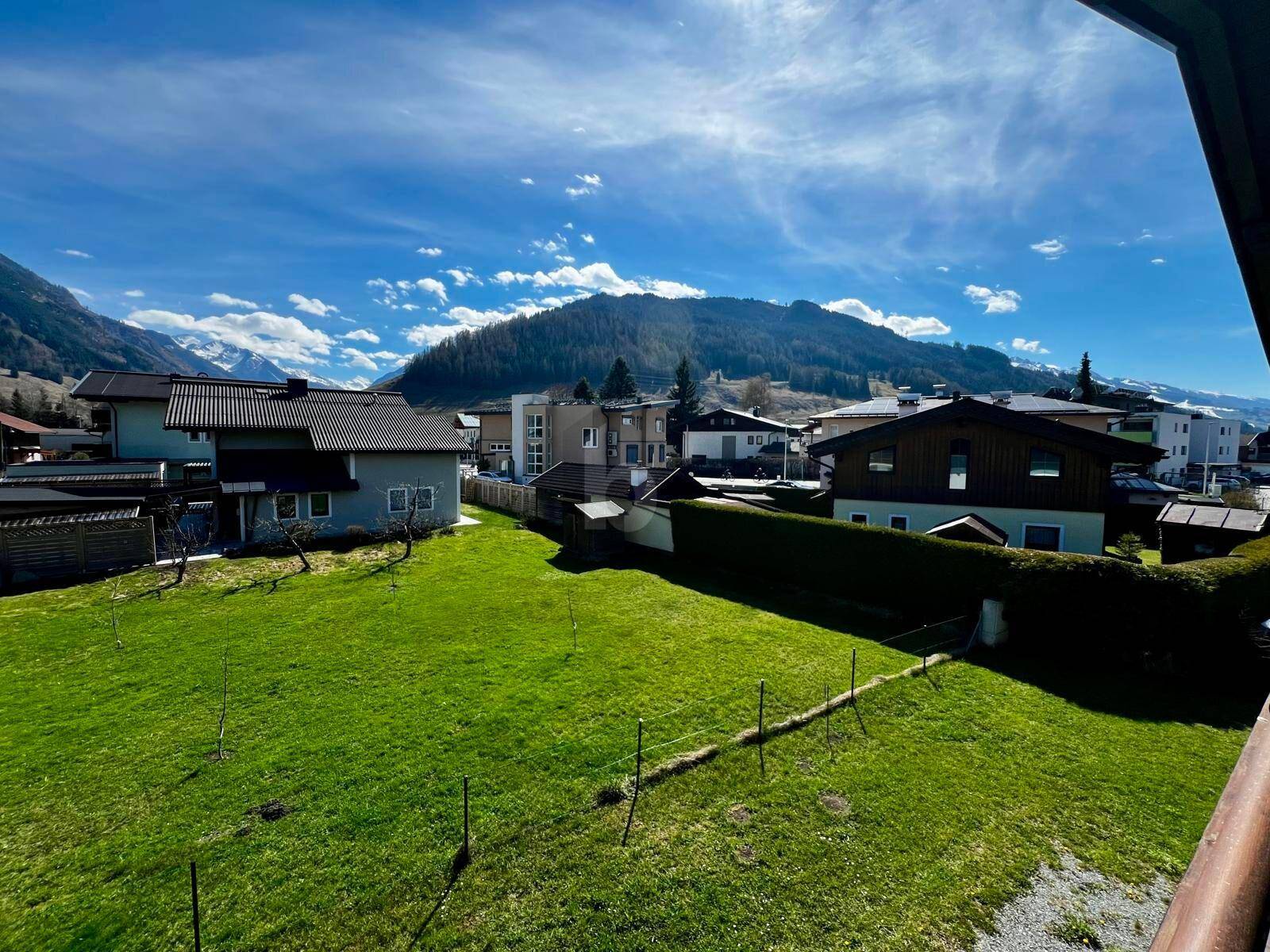 Weitblick über grüne Gärten und Dächer mit majestätischer Berglandschaft im Hintergrund.