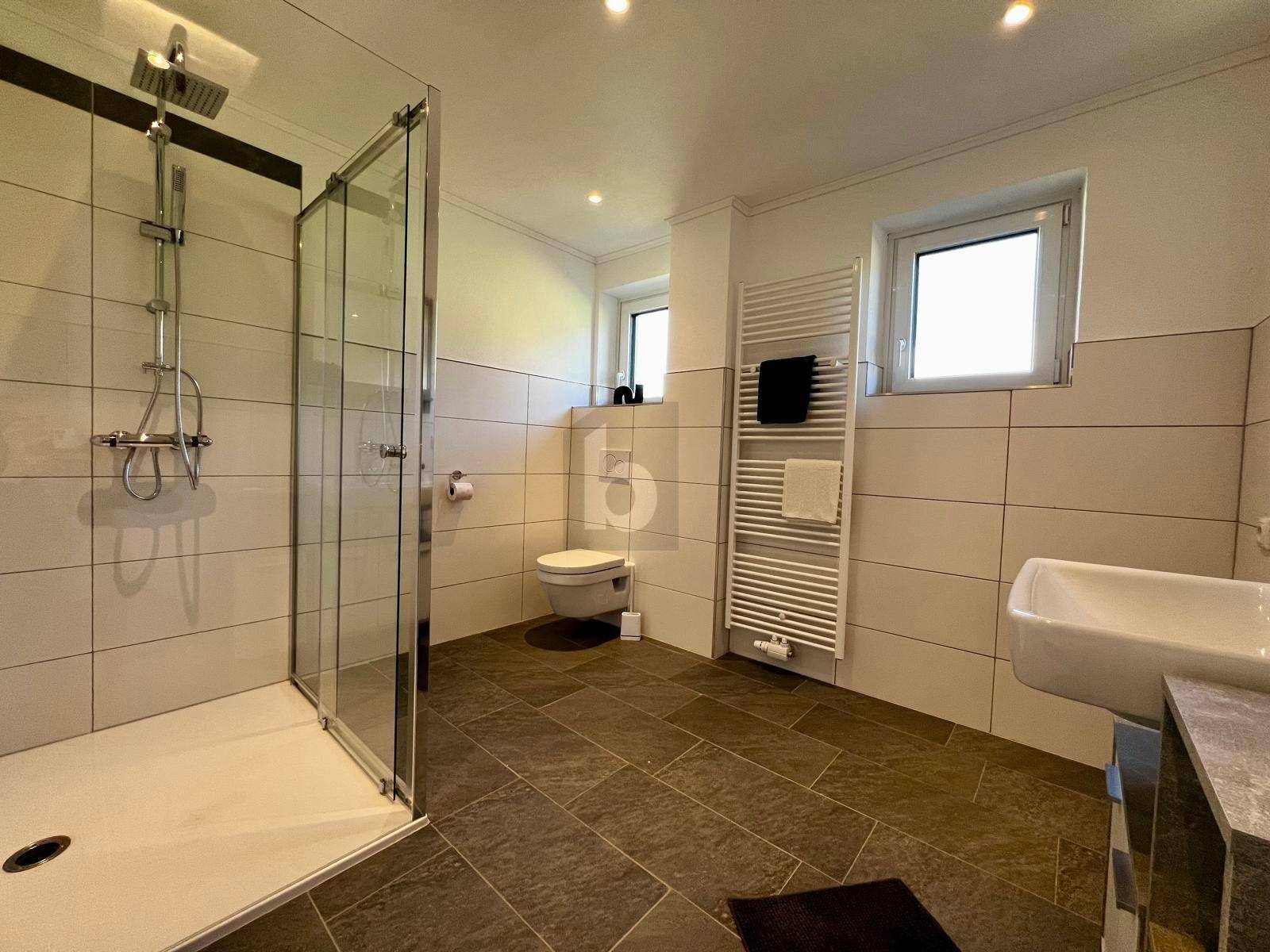 Modernes Badezimmer mit ebenerdiger Dusche, Wand-WC und beheiztem Handtuchhalter.