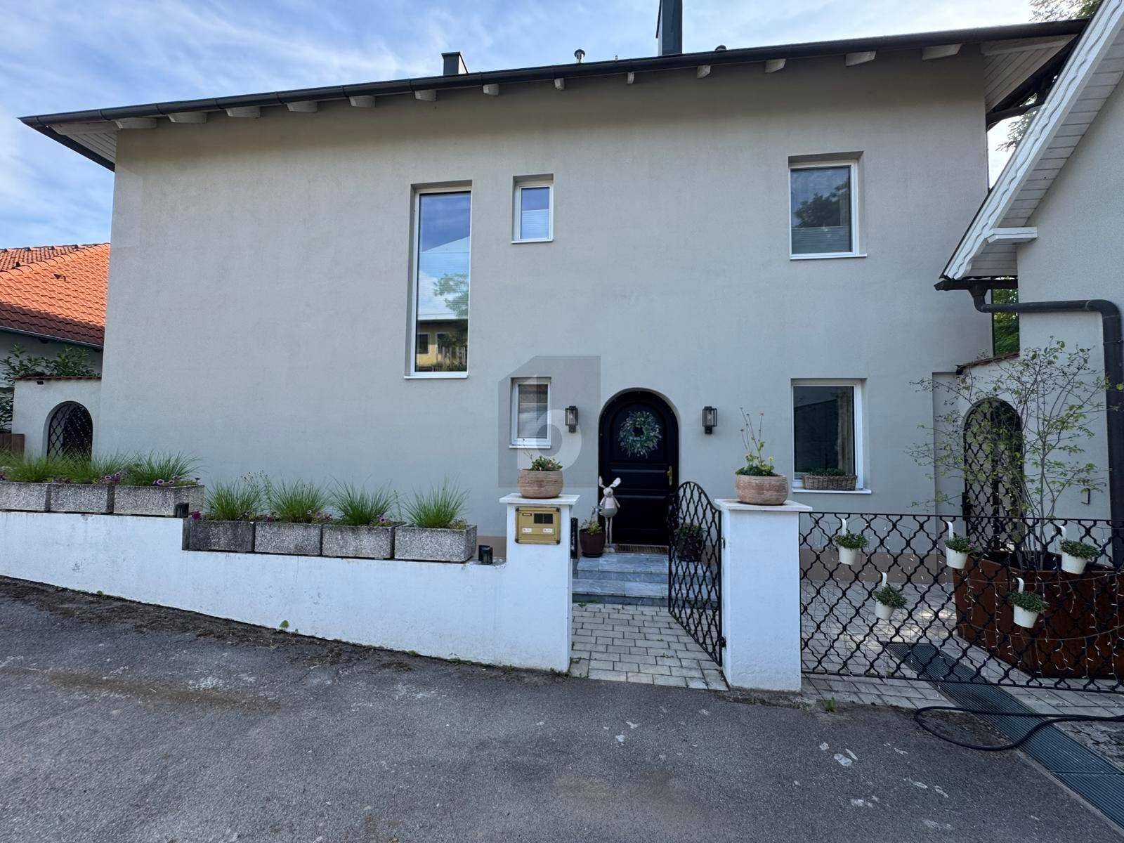 Moderne Hausfassade mit schlichtem Design, großen Fenstern und einem einladenden Eingangsbereich.