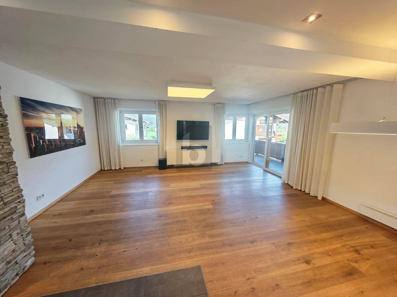 Geräumiges Wohnzimmer mit hellem Holzboden, großen Fenstern und Zugang zum Balkon.