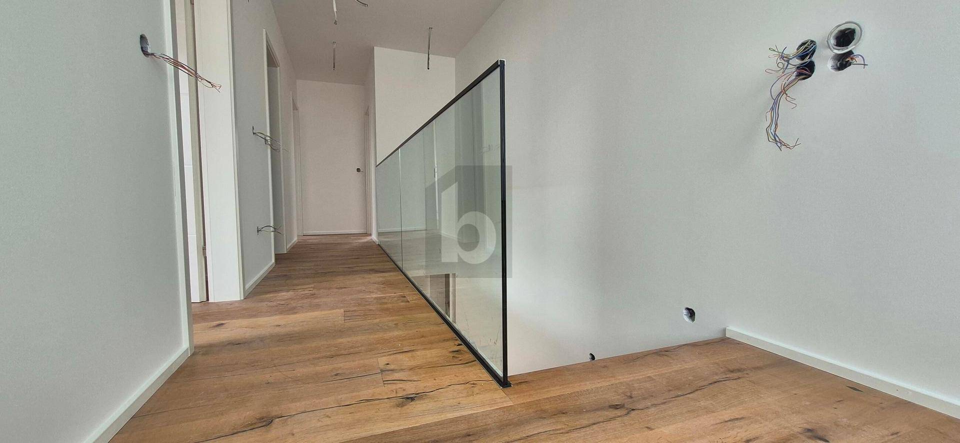 Heller Flur mit Holzboden und modernem Glasgeländer im Obergeschoss.