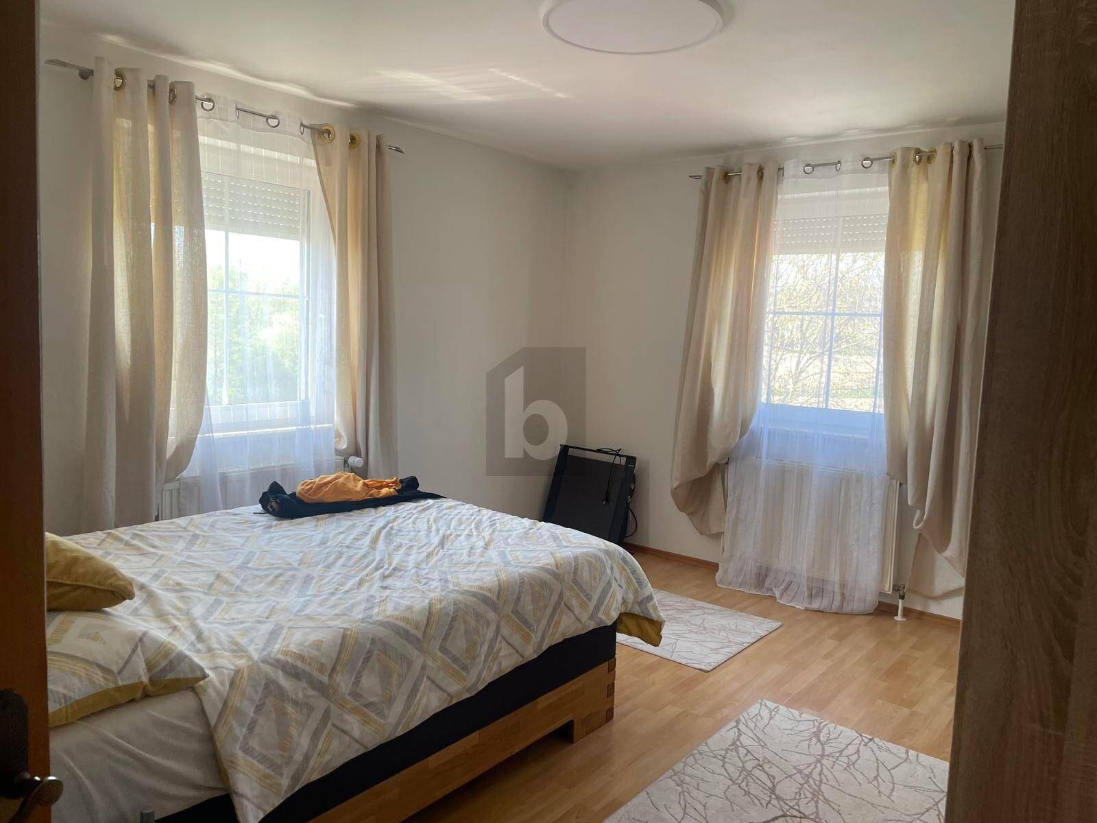Helles Schlafzimmer mit Holzbett, zwei Fenstern und hellem Laminatboden.
