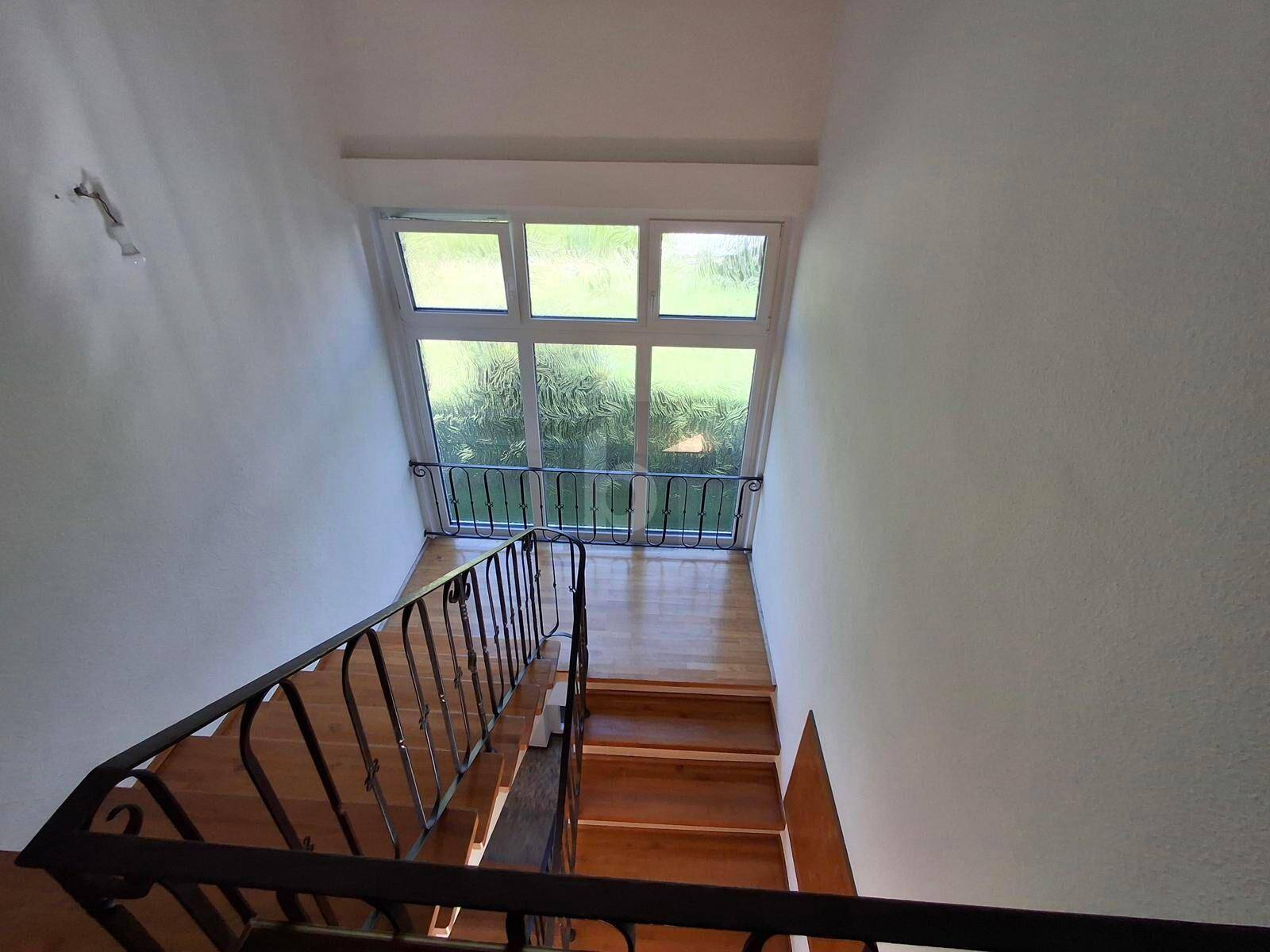 Holztreppe mit schmiedeeisernem Geländer führt zu einem hellen Fenster mit französischem Balkon.