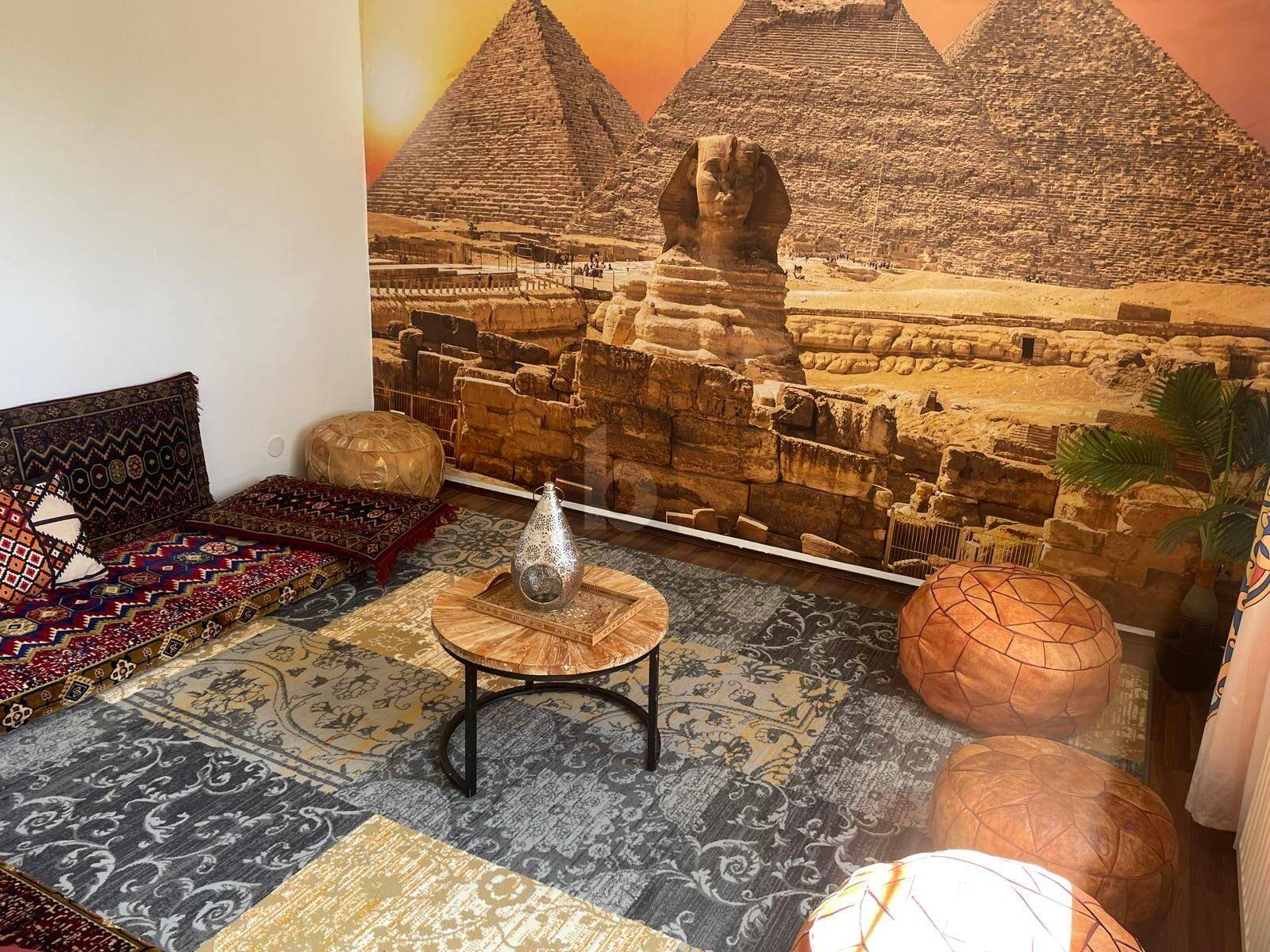 Orientalisch inspiriertes Zimmer mit Wandtapete der Pyramiden, Teppich und Sitzkissen.