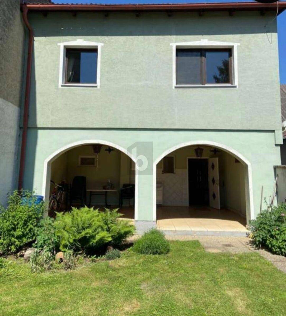 Fassade eines Hauses mit überdachtem Erdgeschoss und grünem Vorgarten.
